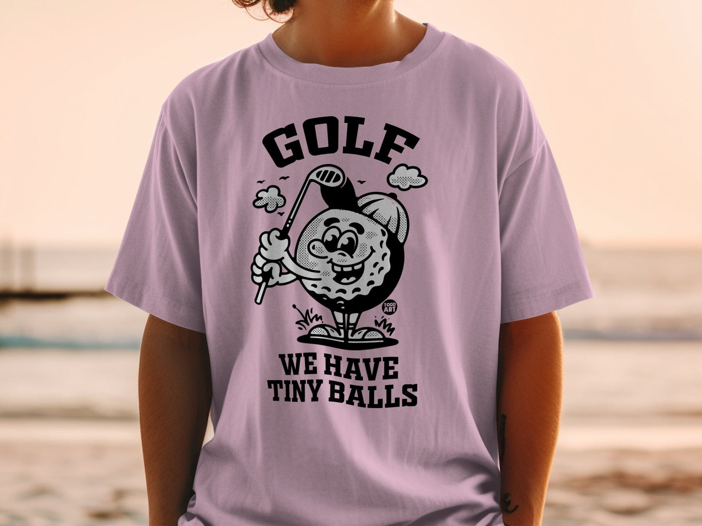 T-shirt with cartoon golf ball swinging club, text "WE HAVE TINY BALLS".