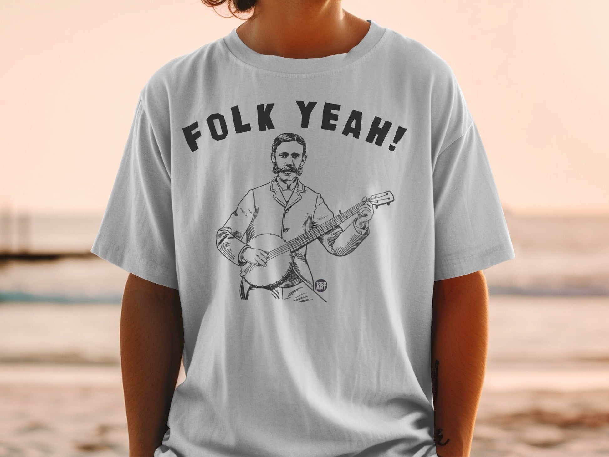 T-shirt featuring a black and white illustration of a man playing a banjo with "FOLK YEAH!" text.