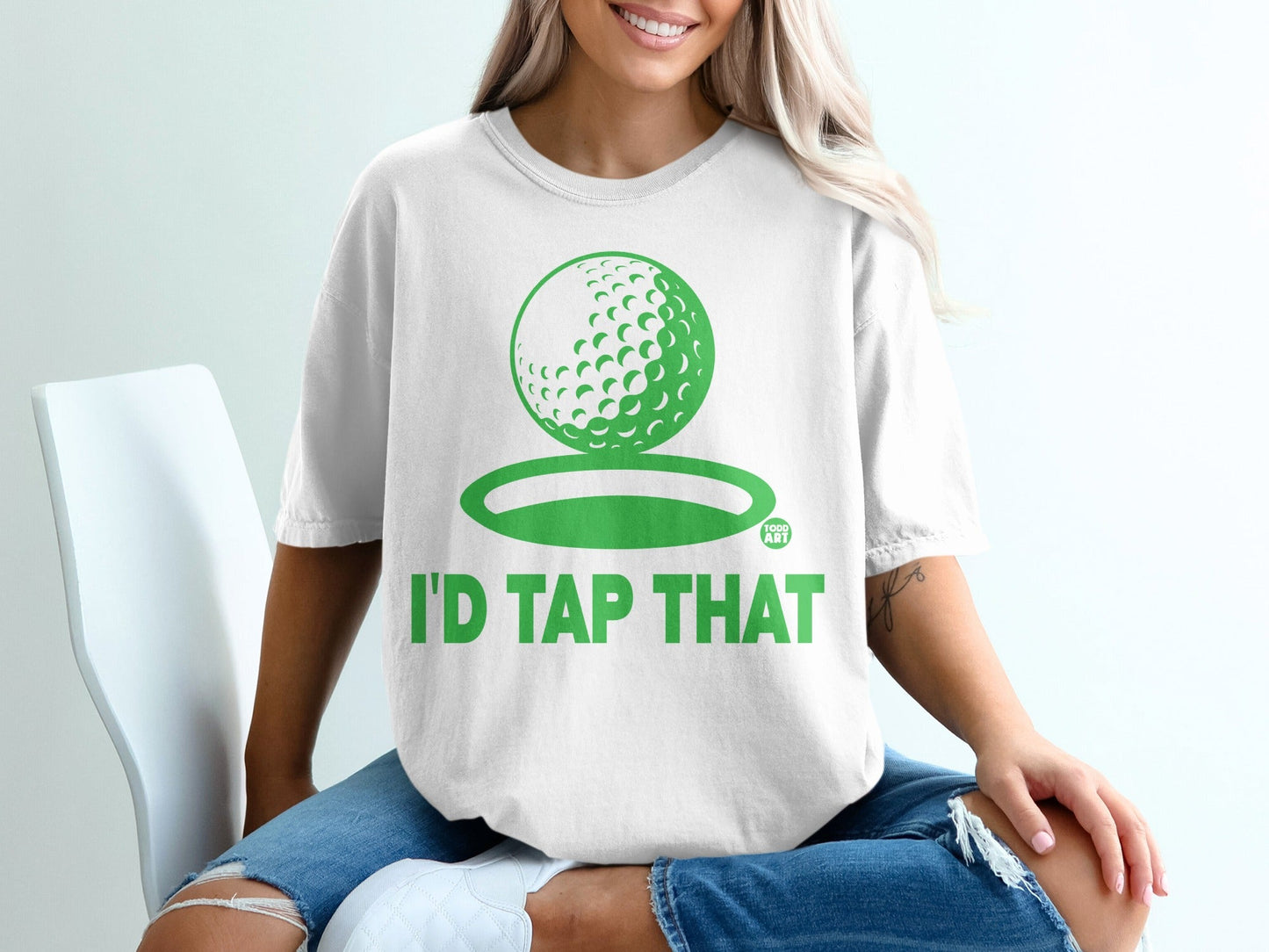 White t-shirt with green golf ball graphic and "I'D TAP THAT" text.