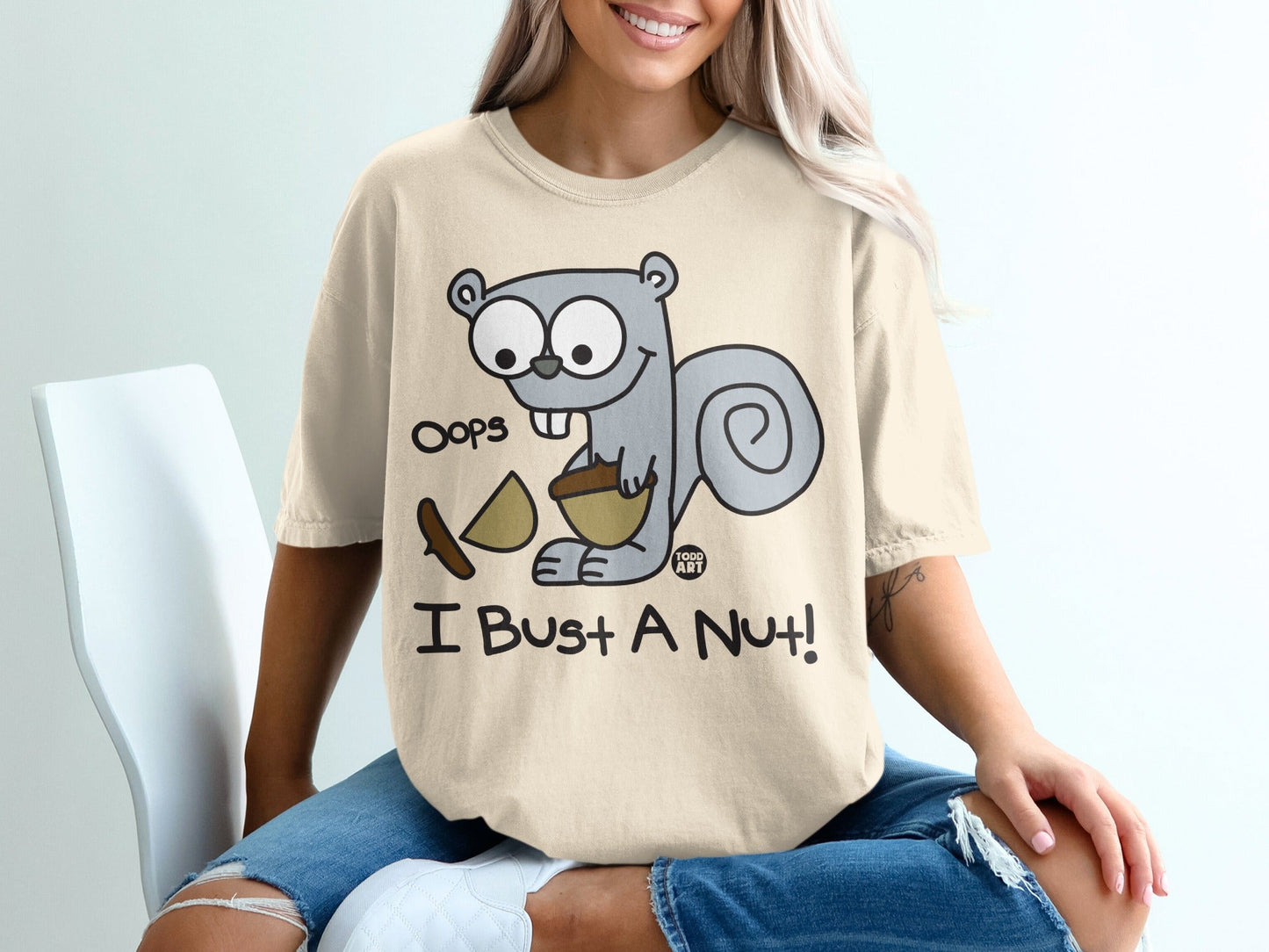 Cream t-shirt with cartoon squirrel holding acorn and text "Oops I Bust A Nut!"