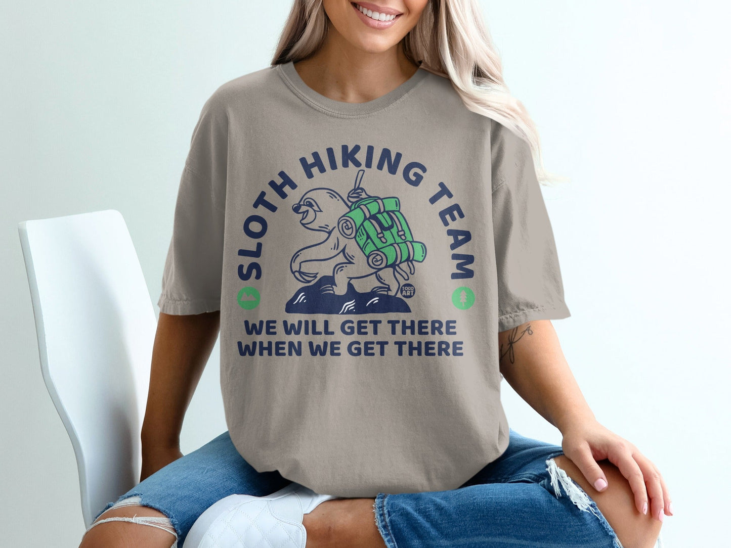 Sloth Hiking Team graphic on a tan t-shirt with a sloth carrying a backpack.