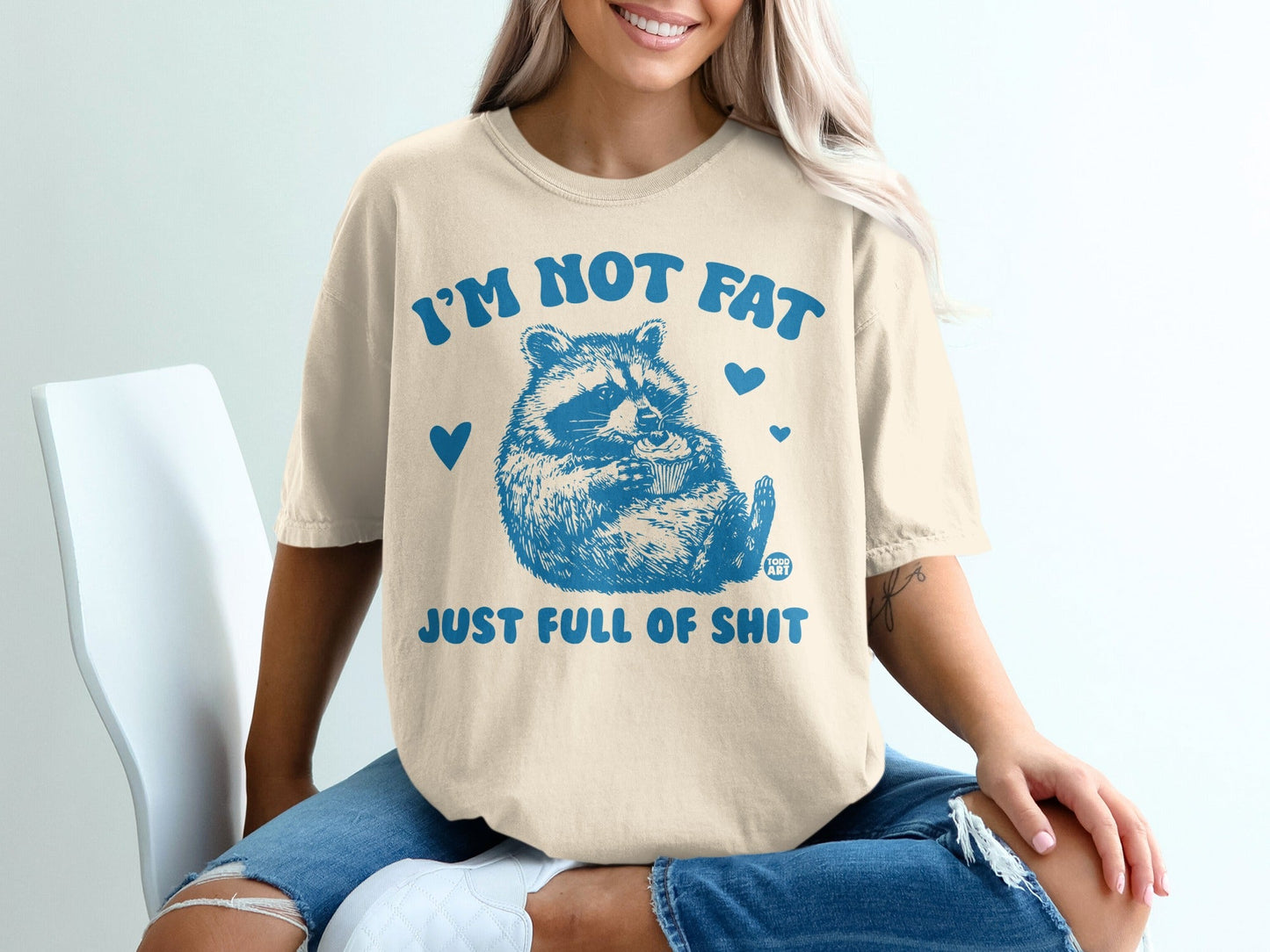 Cream t-shirt with blue raccoon graphic and text "I'M NOT FAT JUST FULL OF SHIT".