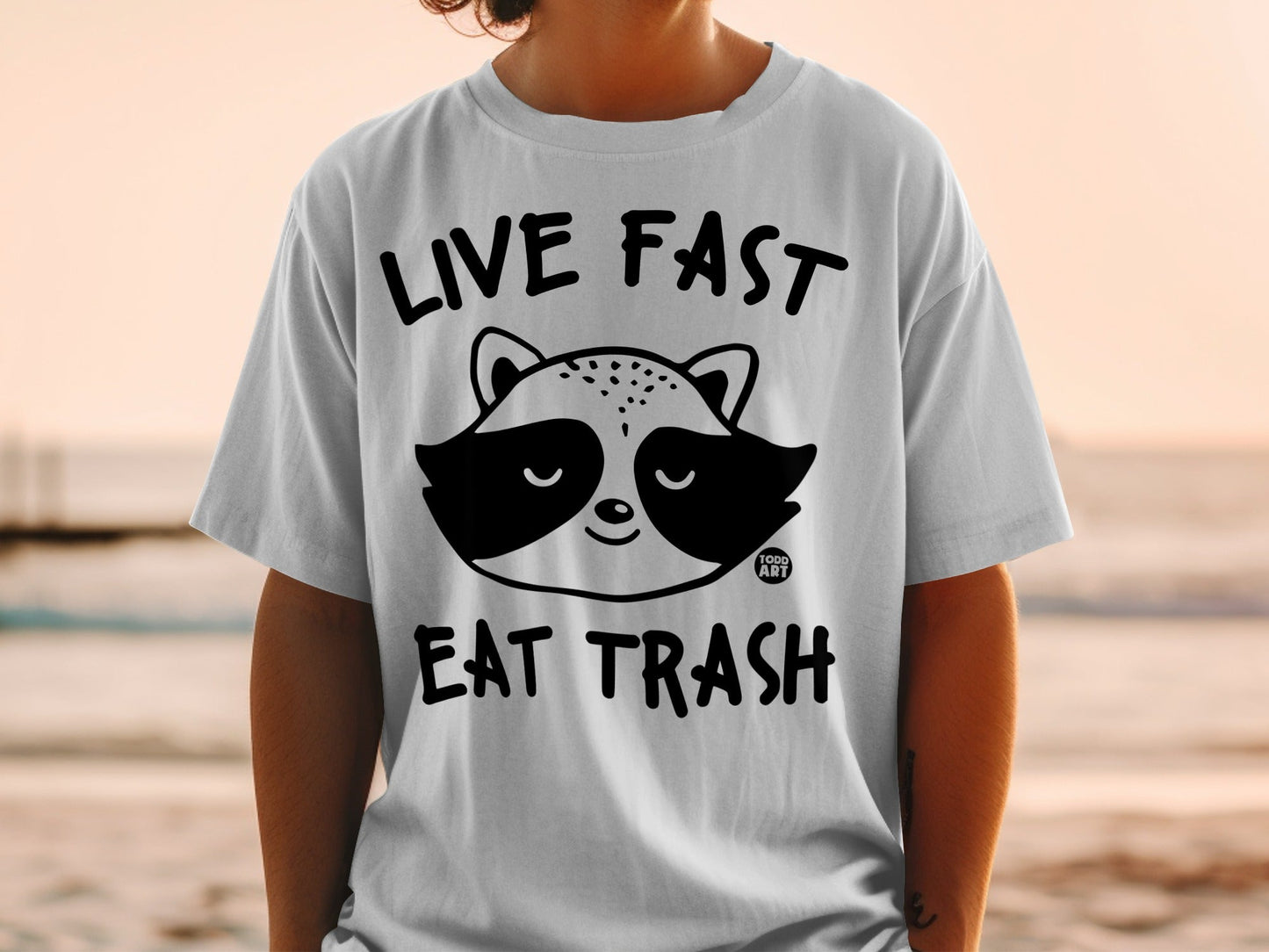 White t-shirt with black graphic of a raccoon and text "LIVE FAST EAT TRASH".