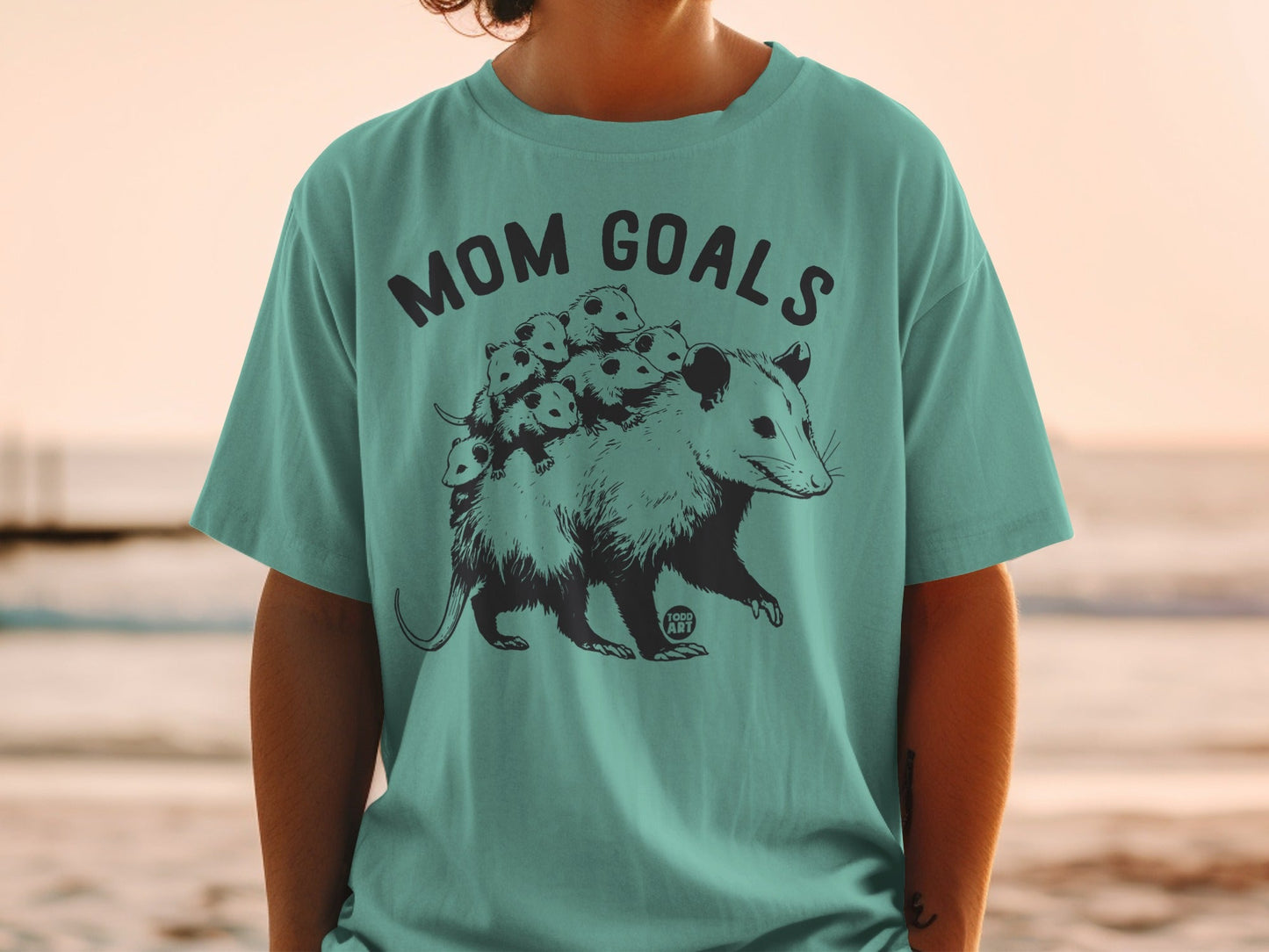 Opossum with babies on back, "Mom Goals" text on teal t-shirt.