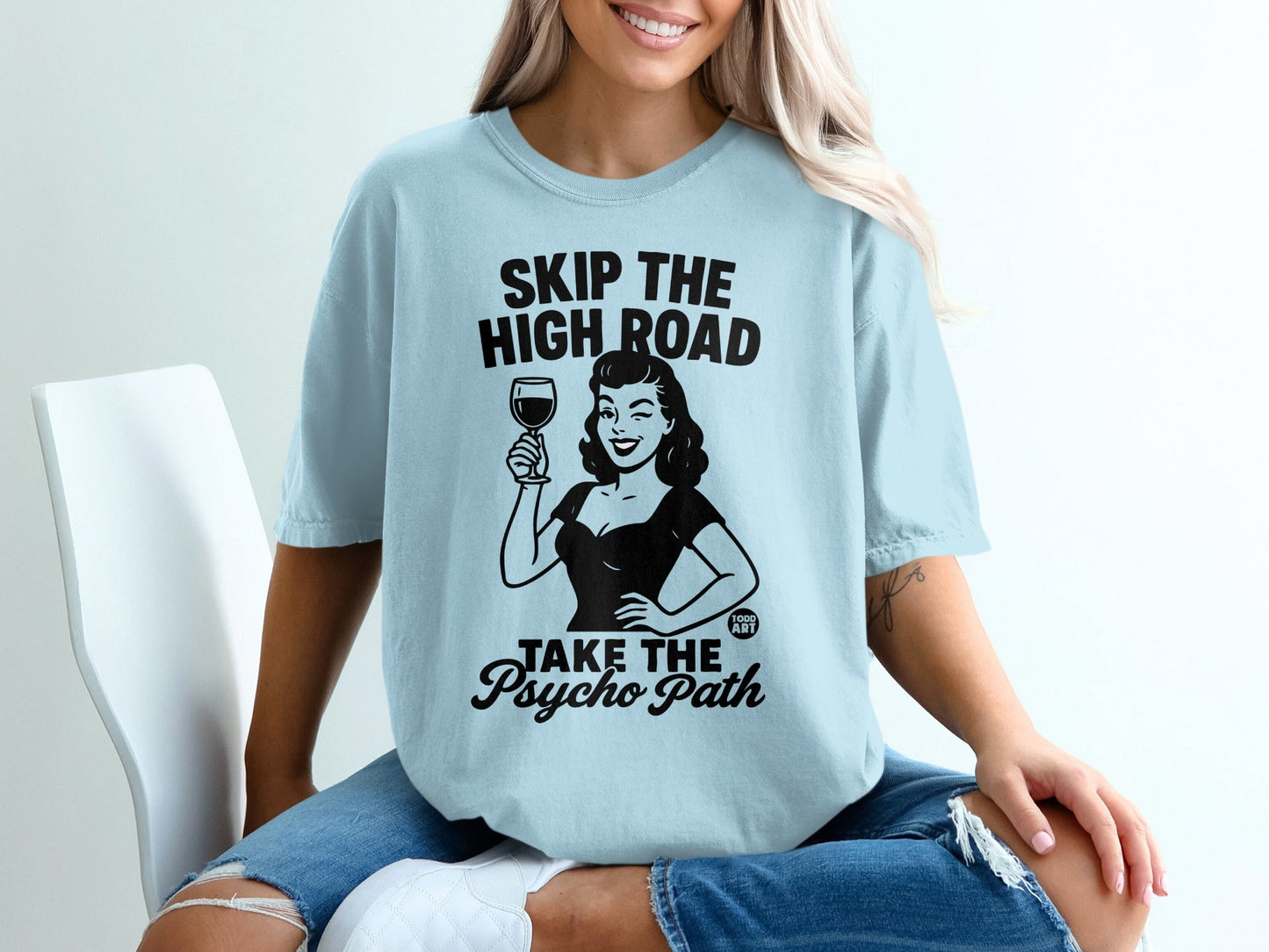 Light blue t-shirt with black graphic of woman holding wine glass, text "SKIP THE HIGH ROAD TAKE THE PSYCHO PATH".