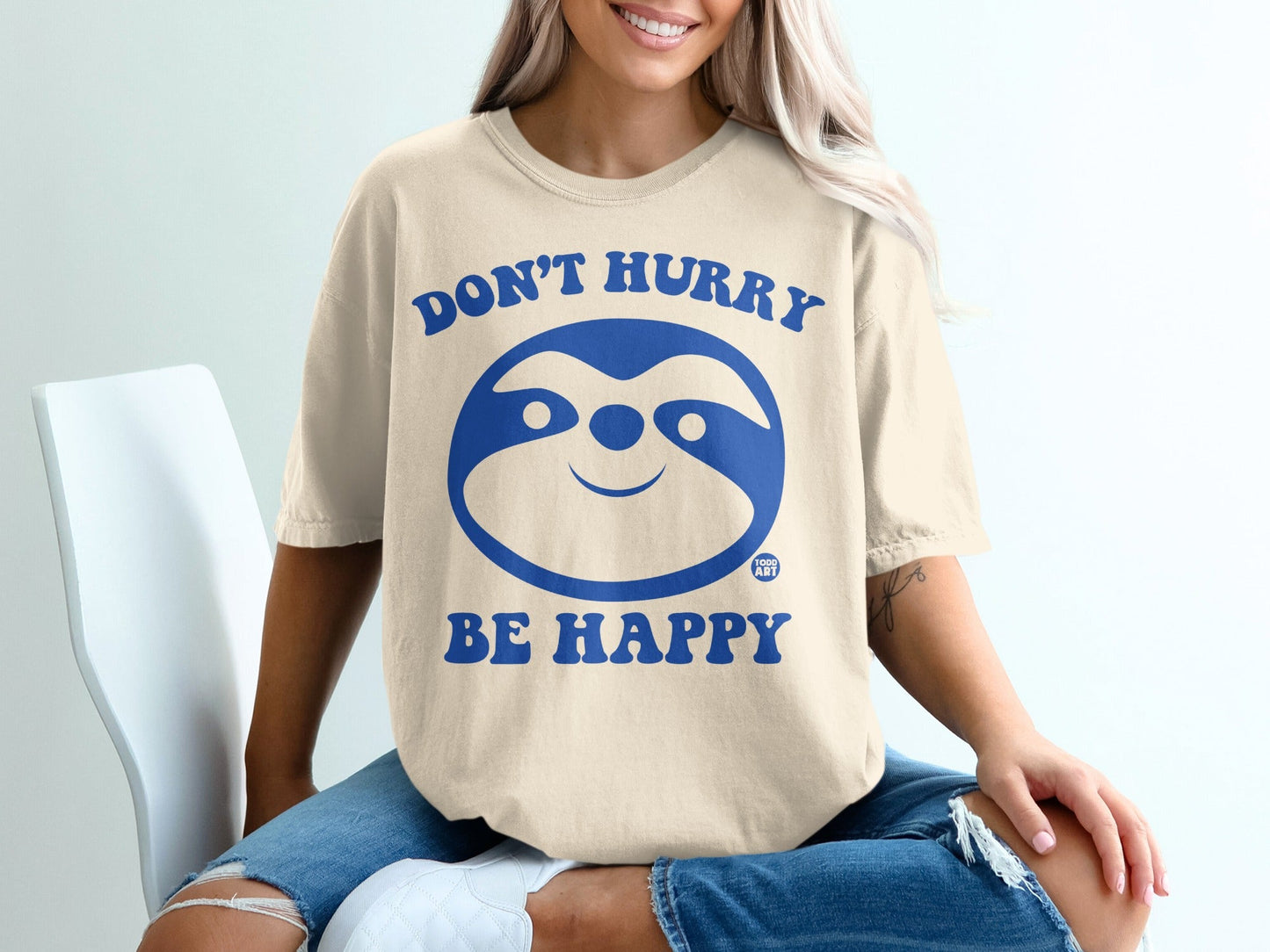 Cream t-shirt with blue sloth graphic and text "DON'T HURRY BE HAPPY."