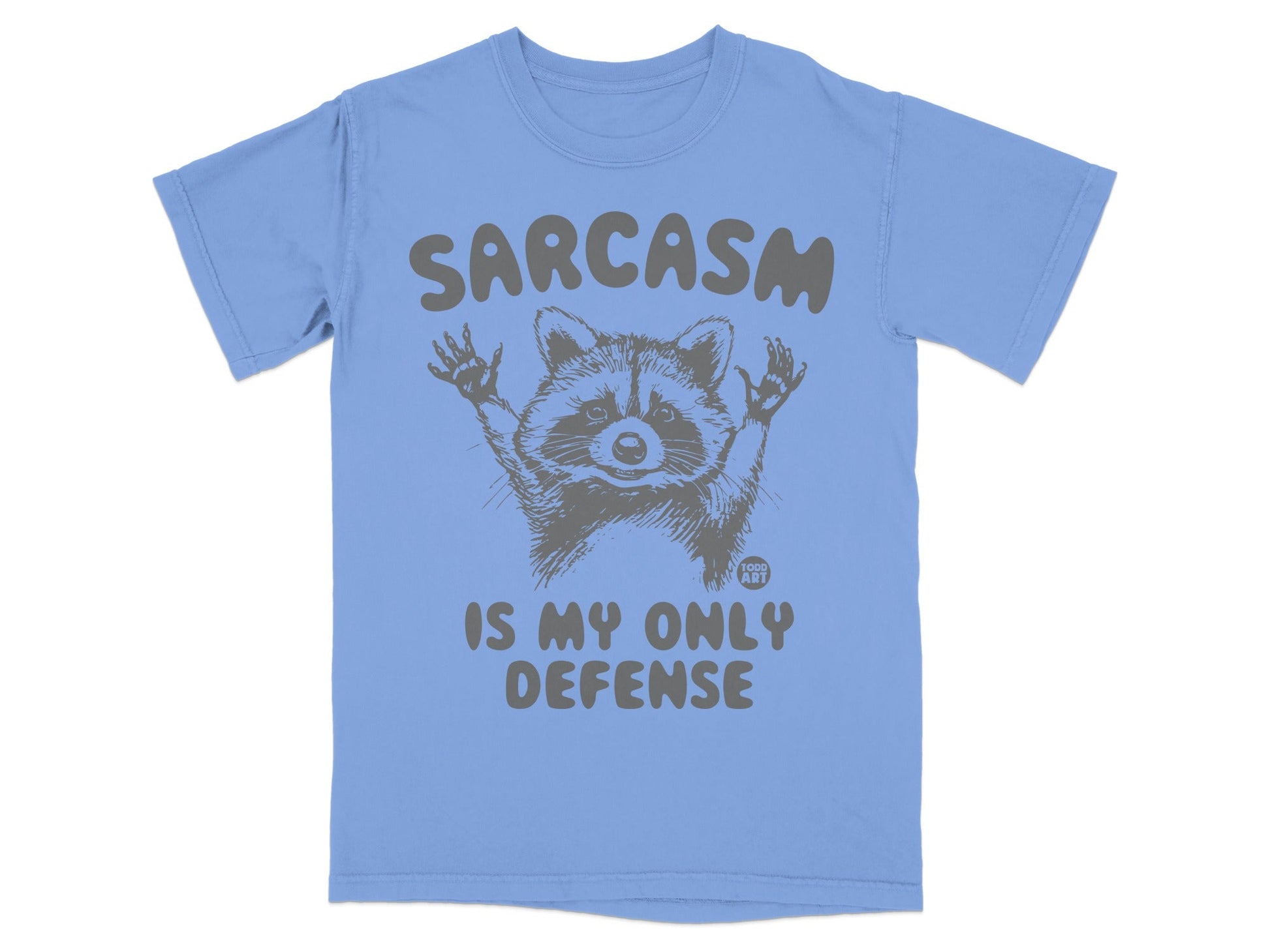 Light blue t-shirt with raccoon graphic and "Sarcasm is my only defense" text.