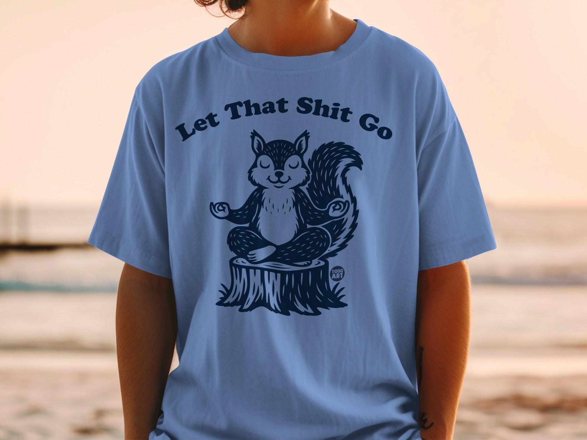 T-shirt with illustration of a meditating squirrel on a tree stump, text "Let That Shit Go".