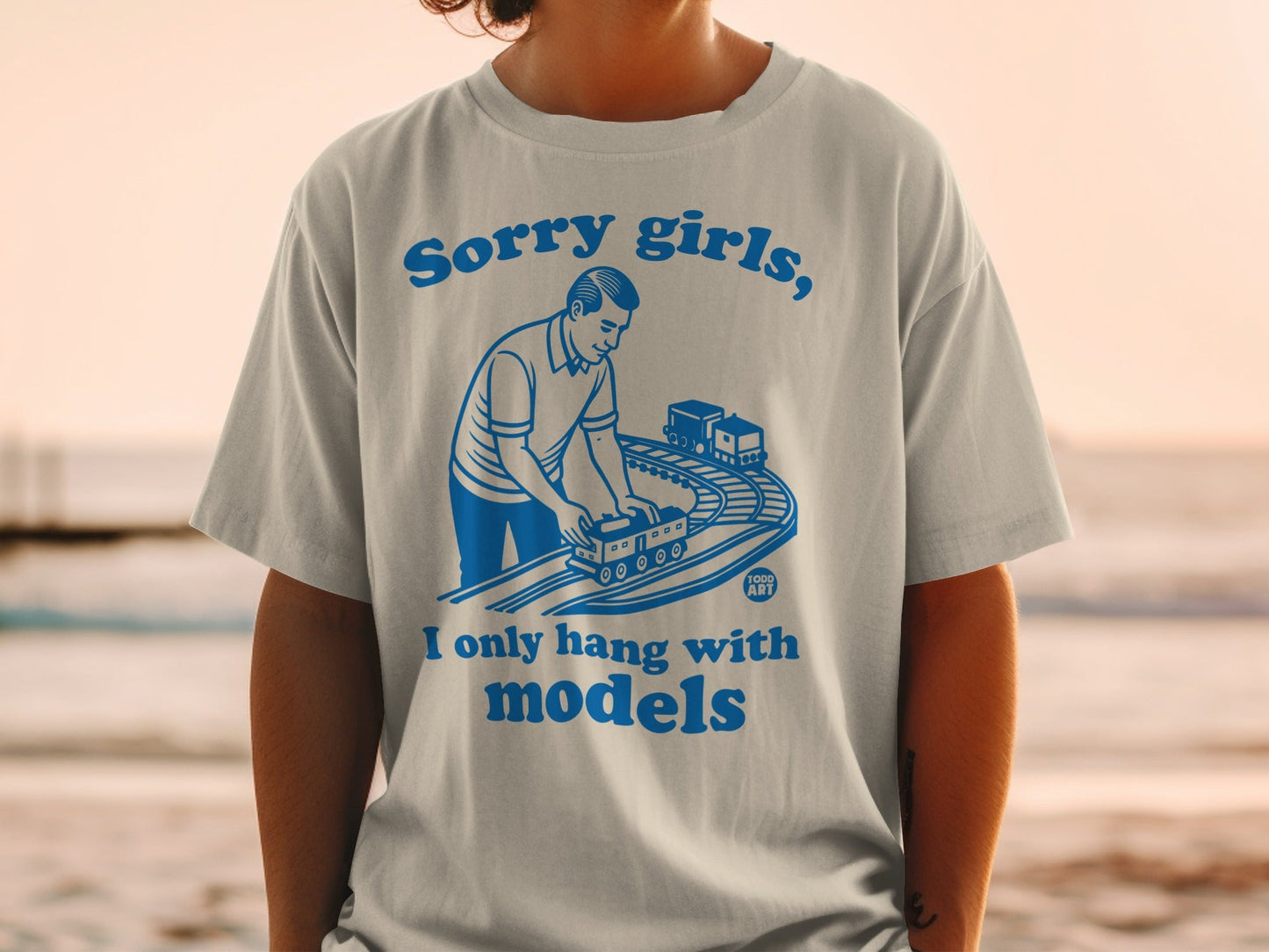 White t-shirt with blue graphic of man playing with model train.