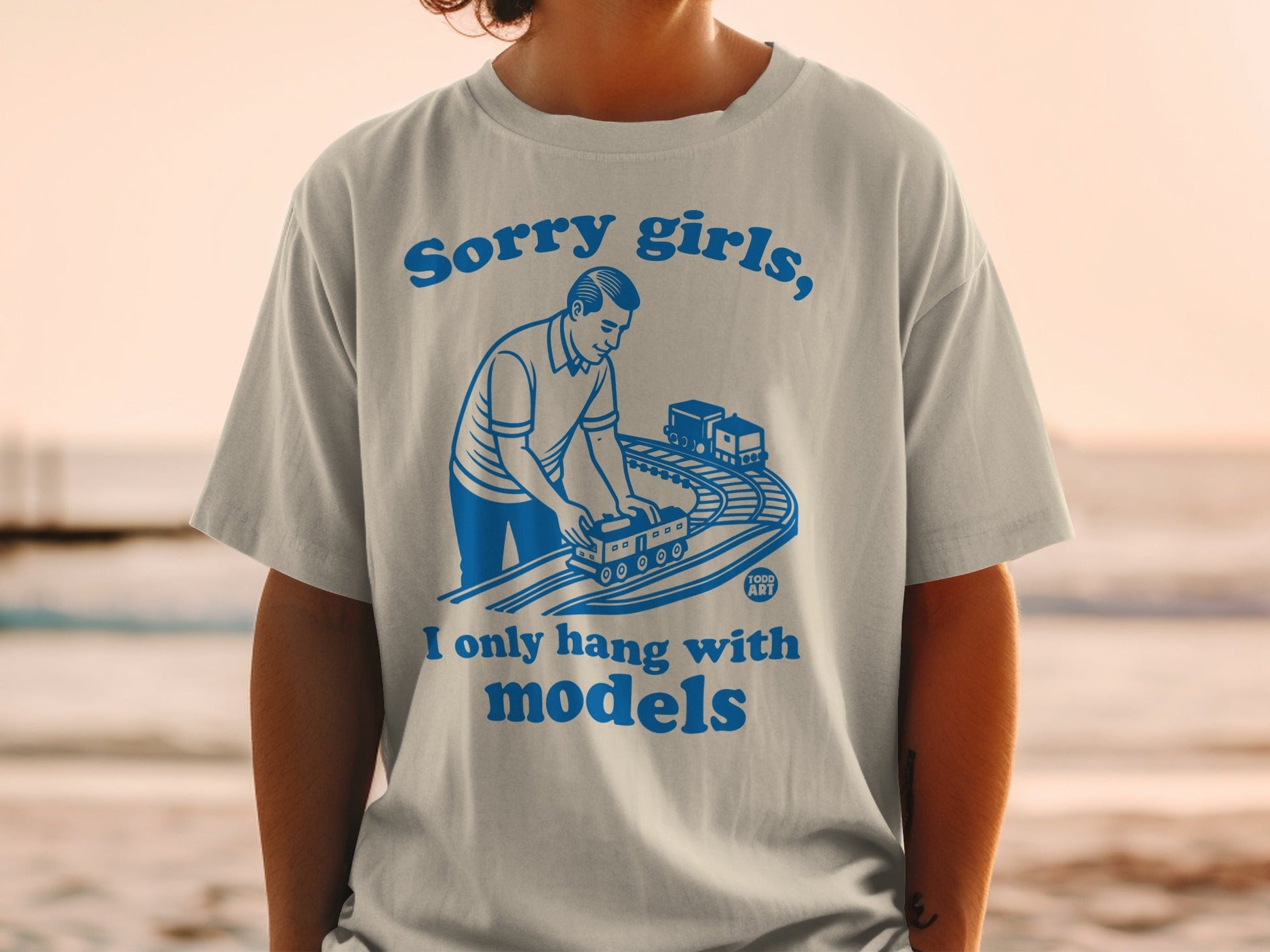 White t-shirt with blue graphic of man playing with model train.