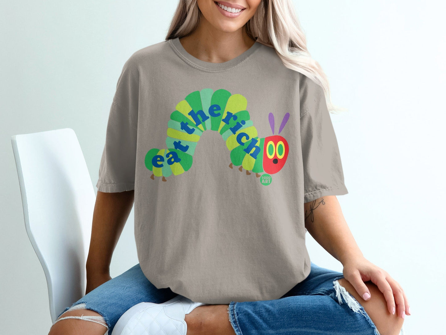 Green caterpillar graphic with "eat the rich" text on a tan t-shirt.