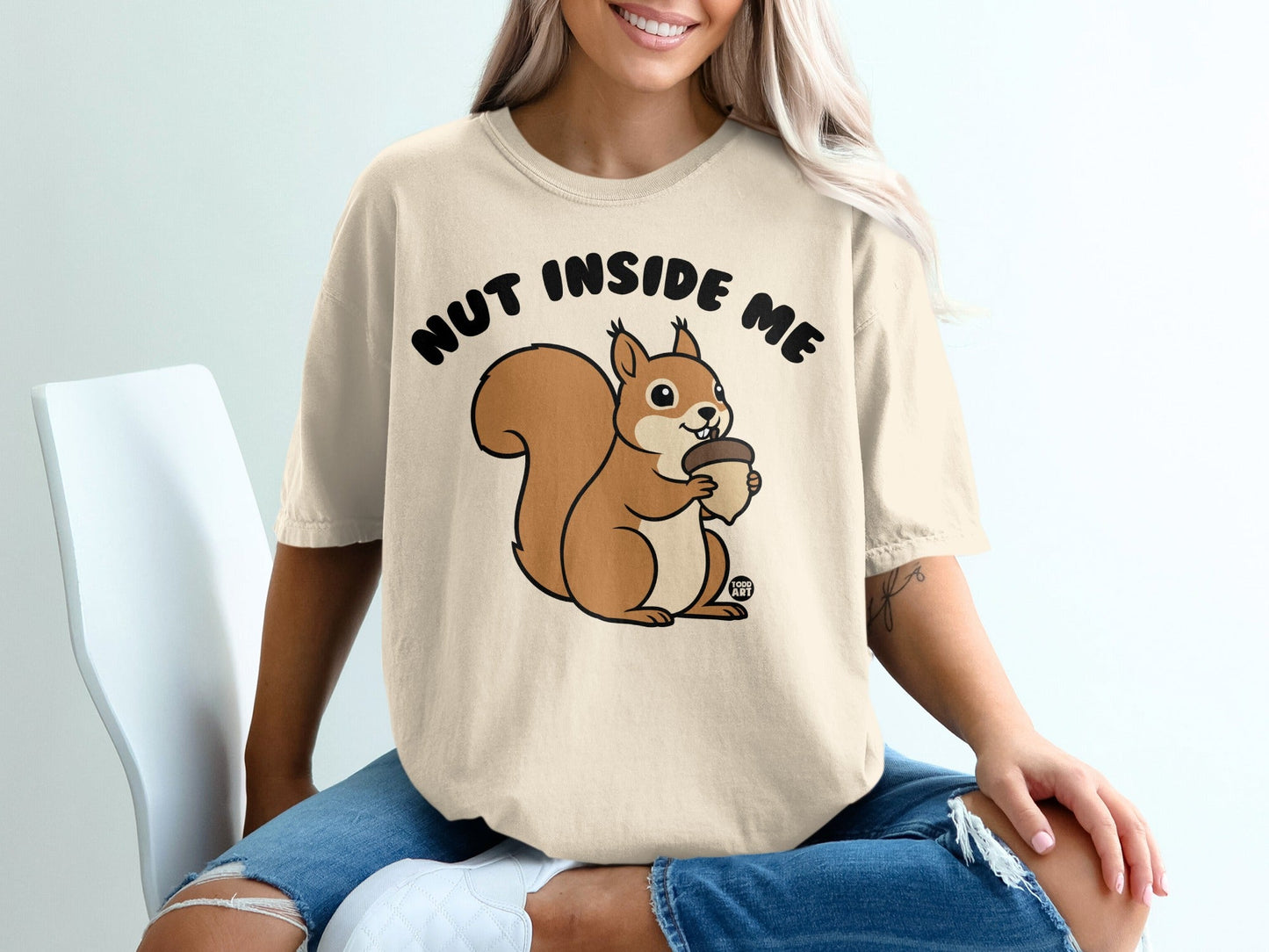 Cream t-shirt with a cartoon squirrel holding an acorn, text "NUT INSIDE ME".