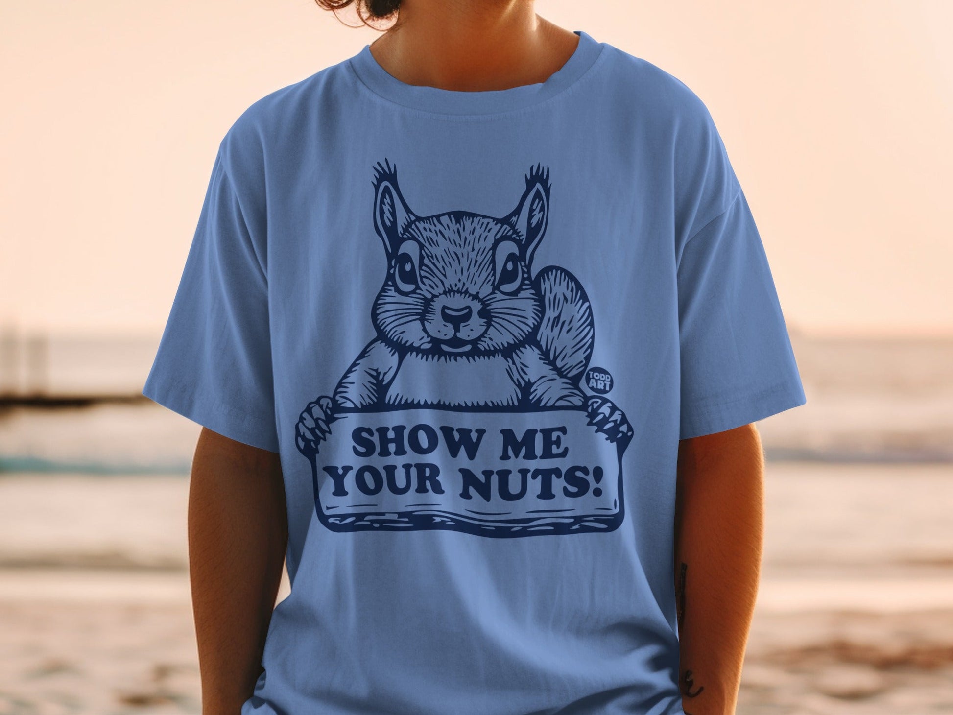 Blue t-shirt with a squirrel holding a sign that says "SHOW ME YOUR NUTS!".