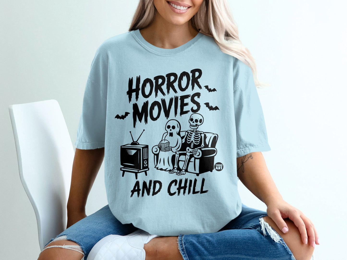 Light blue t-shirt with skeleton and ghost watching TV, "Horror Movies and Chill" text.