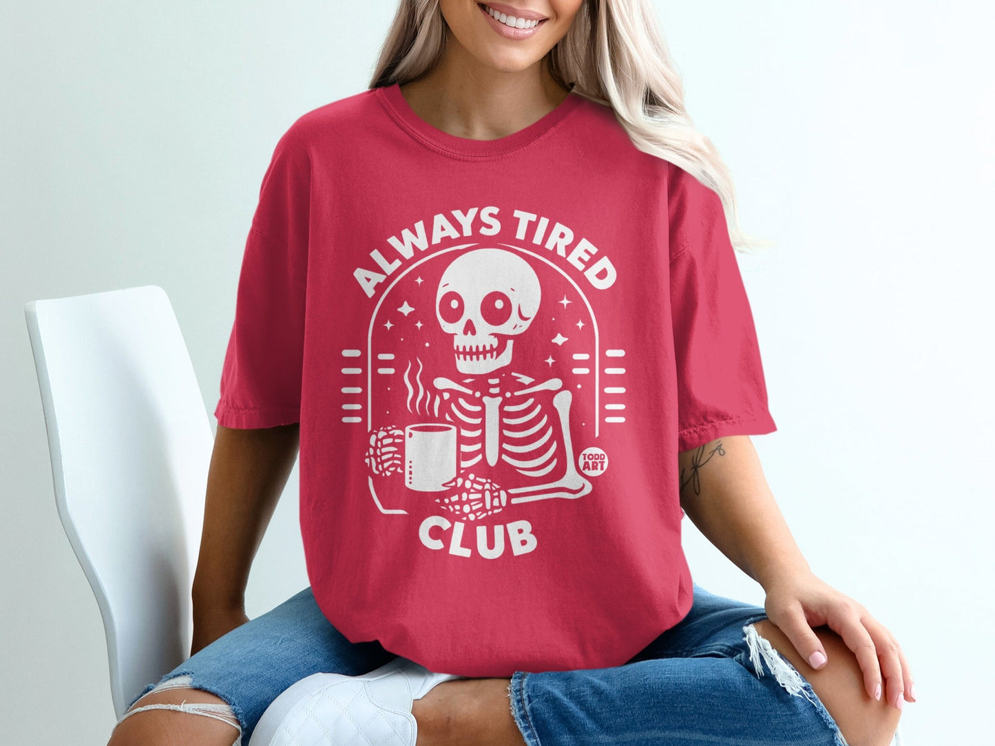 Skeleton in red t-shirt with "Always Tired Club" and coffee mug graphic.