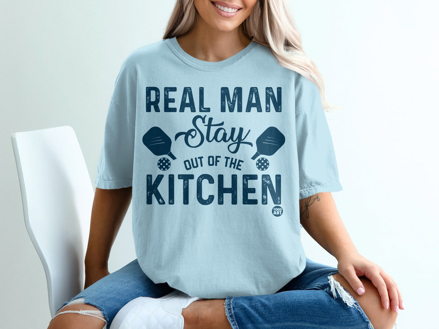 Light blue t-shirt with "Real Man Stay Out of the Kitchen" text and pickleball paddles.