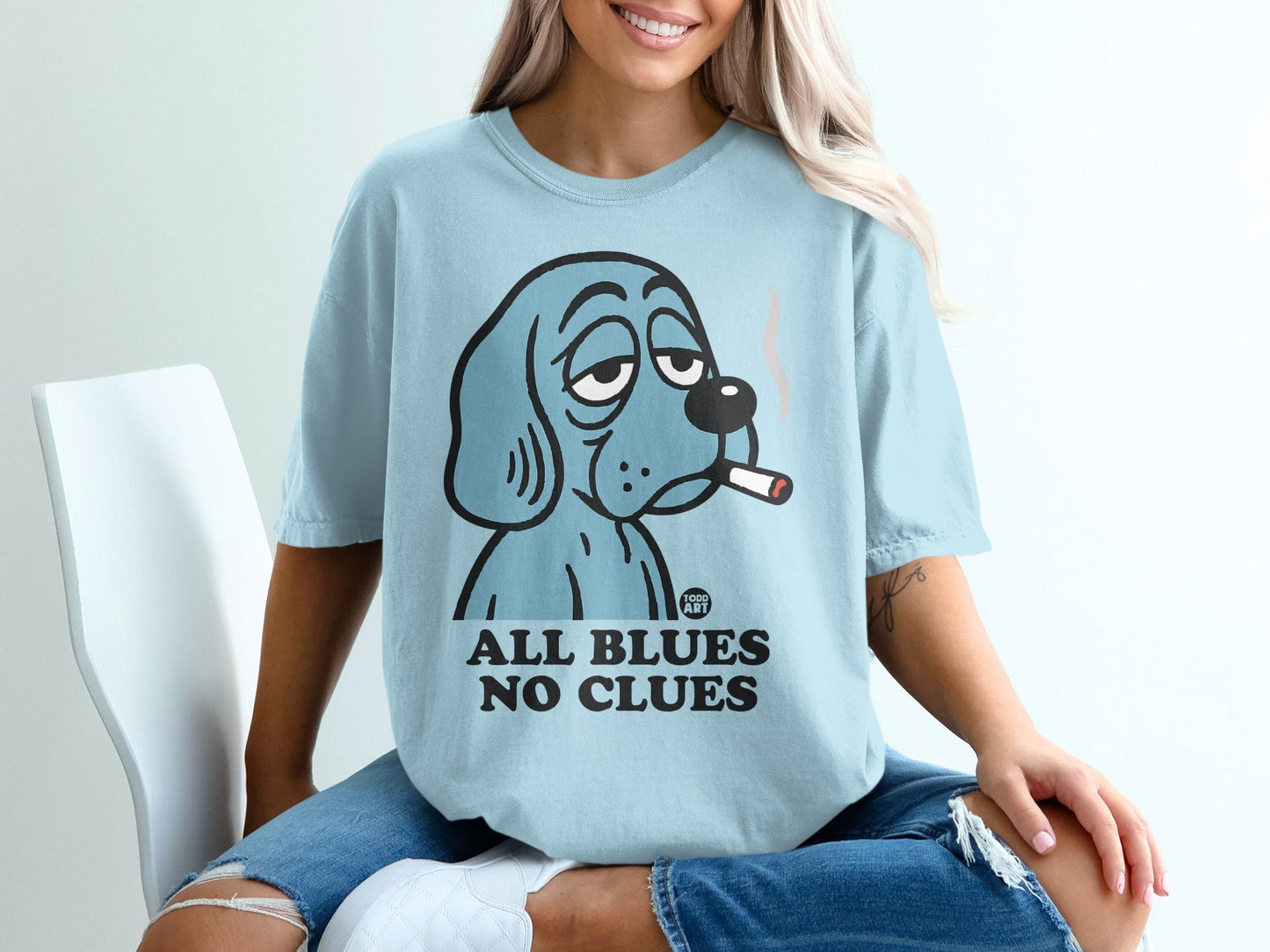 Blue dog with cigarette on light blue t-shirt, text "ALL BLUES NO CLUES".
