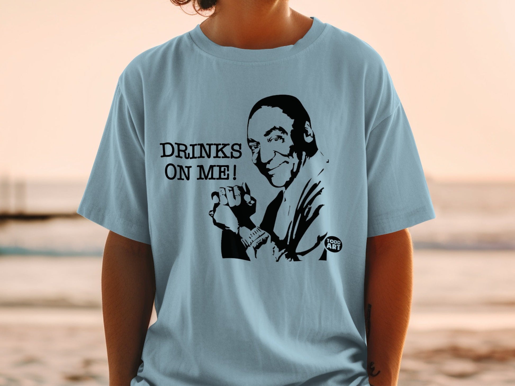Light blue t-shirt with "DRINKS ON ME!" and caricature of a man.