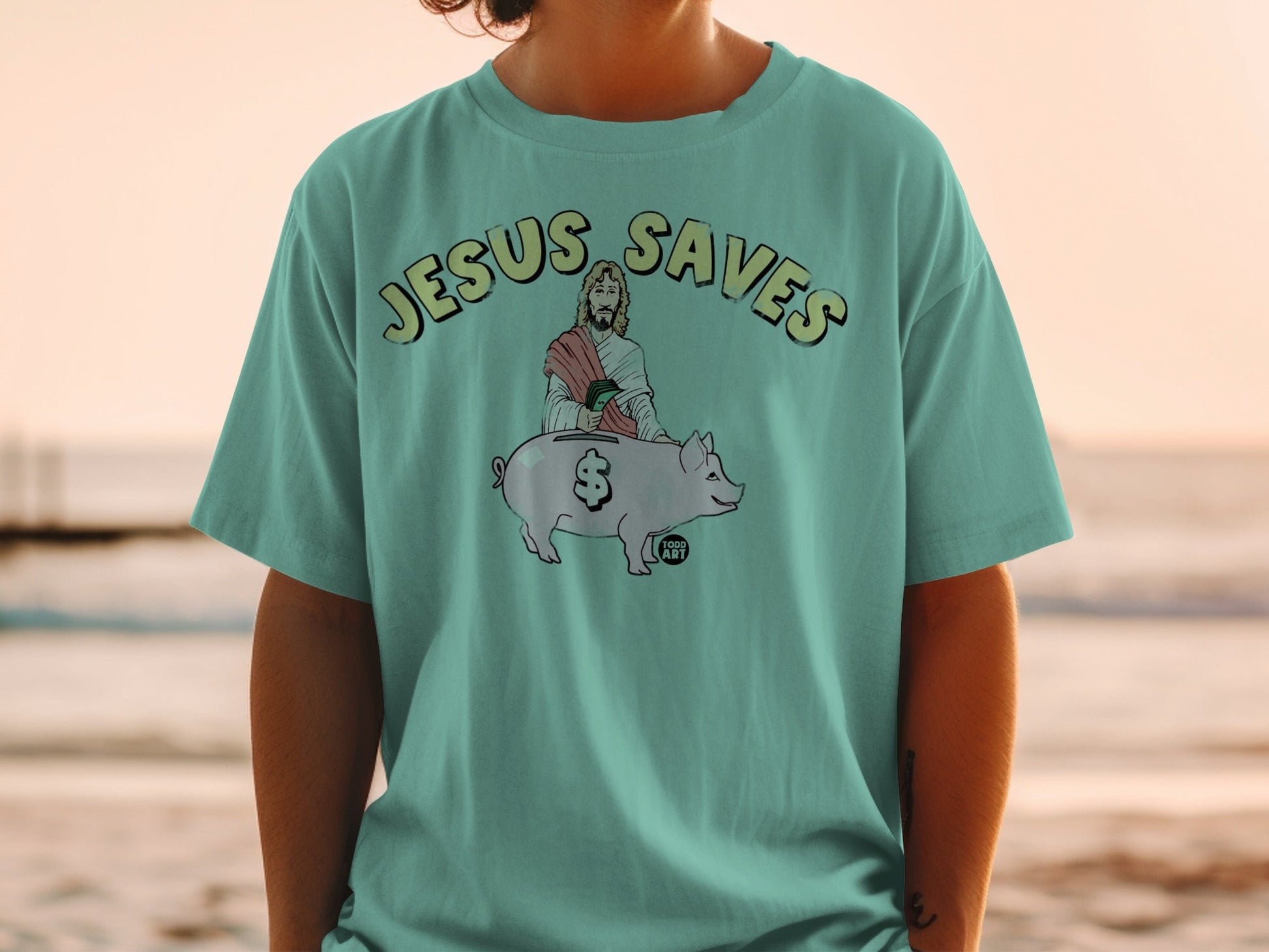 Teal t-shirt with "Jesus Saves" text and Jesus holding a piggy bank.