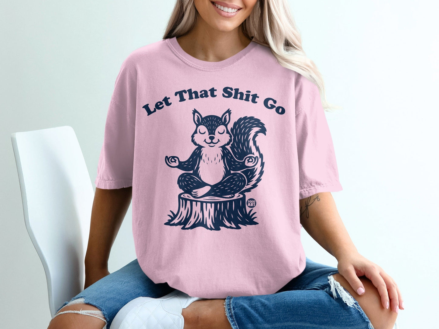 Pink t-shirt with "Let That Shit Go" and a meditating squirrel on a tree stump.