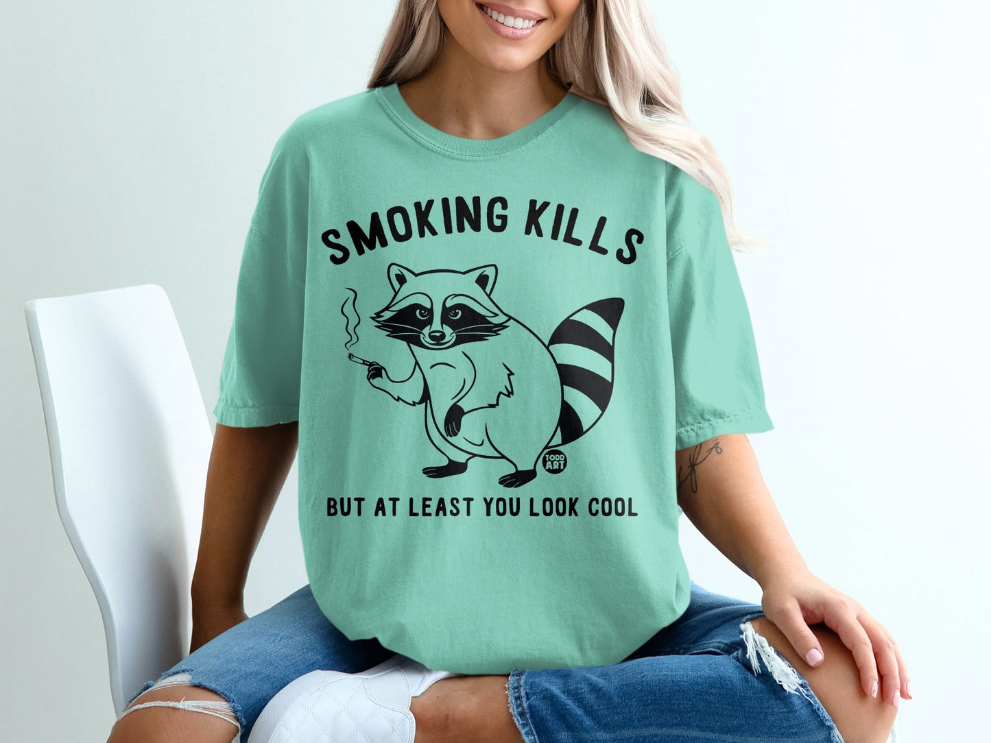 Mint t-shirt with raccoon smoking, text "Smoking kills but at least you look cool".