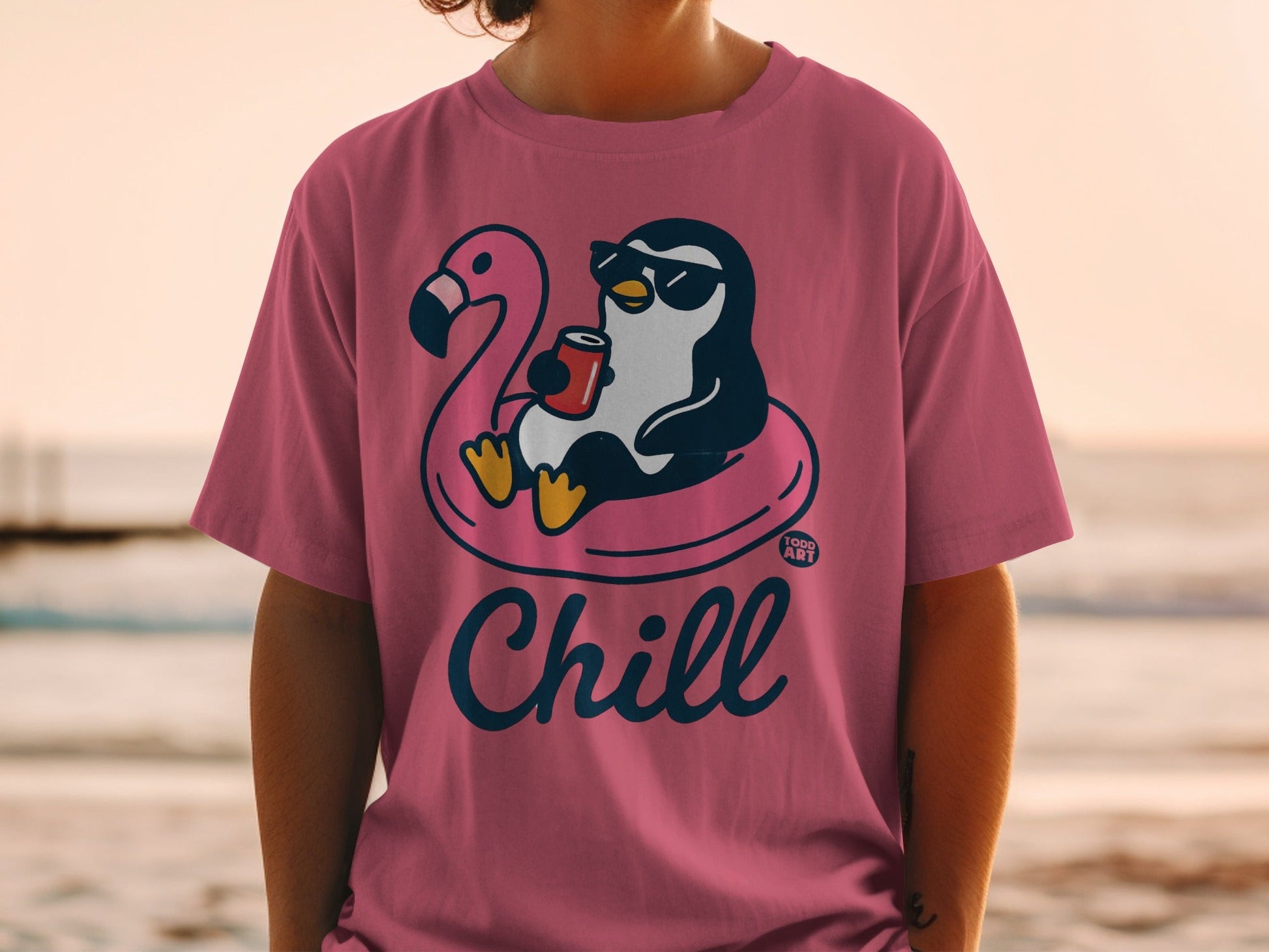Pink t-shirt with a cartoon penguin on a flamingo float holding a drink, text "Chill".