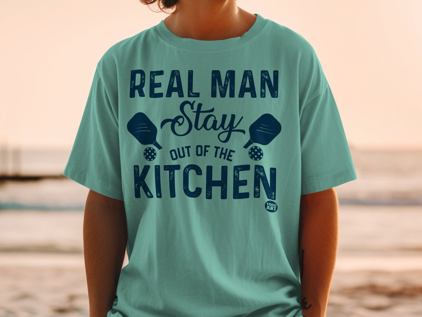 Teal t-shirt with "Real Man Stay Out of the Kitchen" and pickleball paddles.