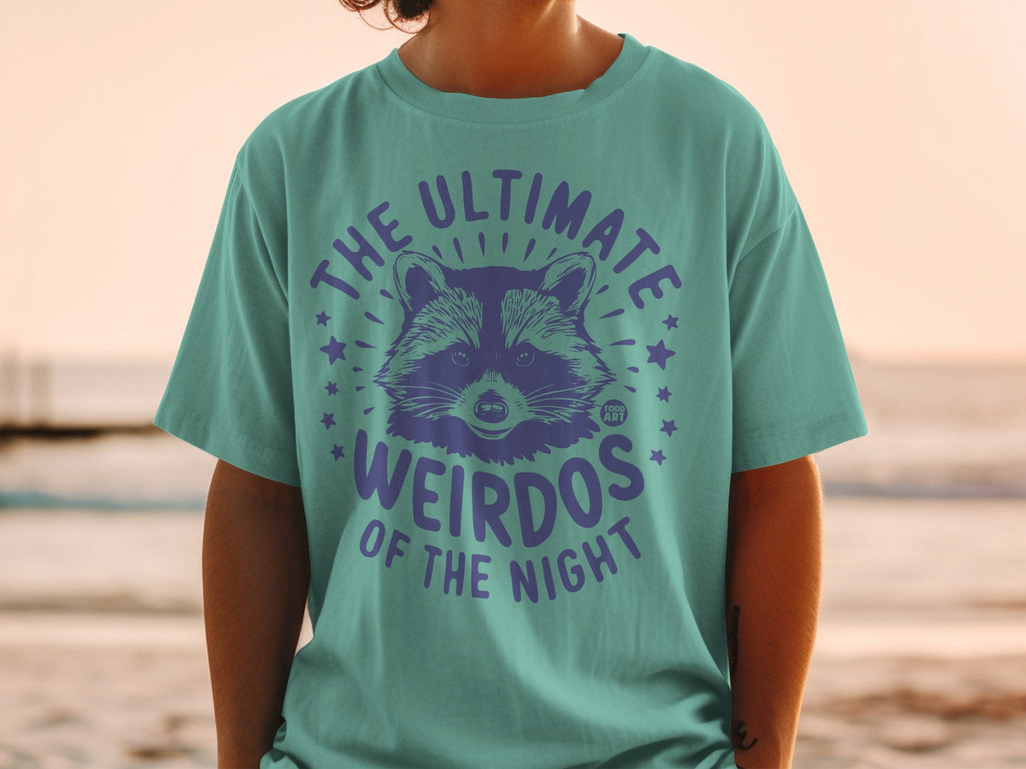 Teal t-shirt with purple raccoon graphic and "The Ultimate Weirdos of the Night" text.