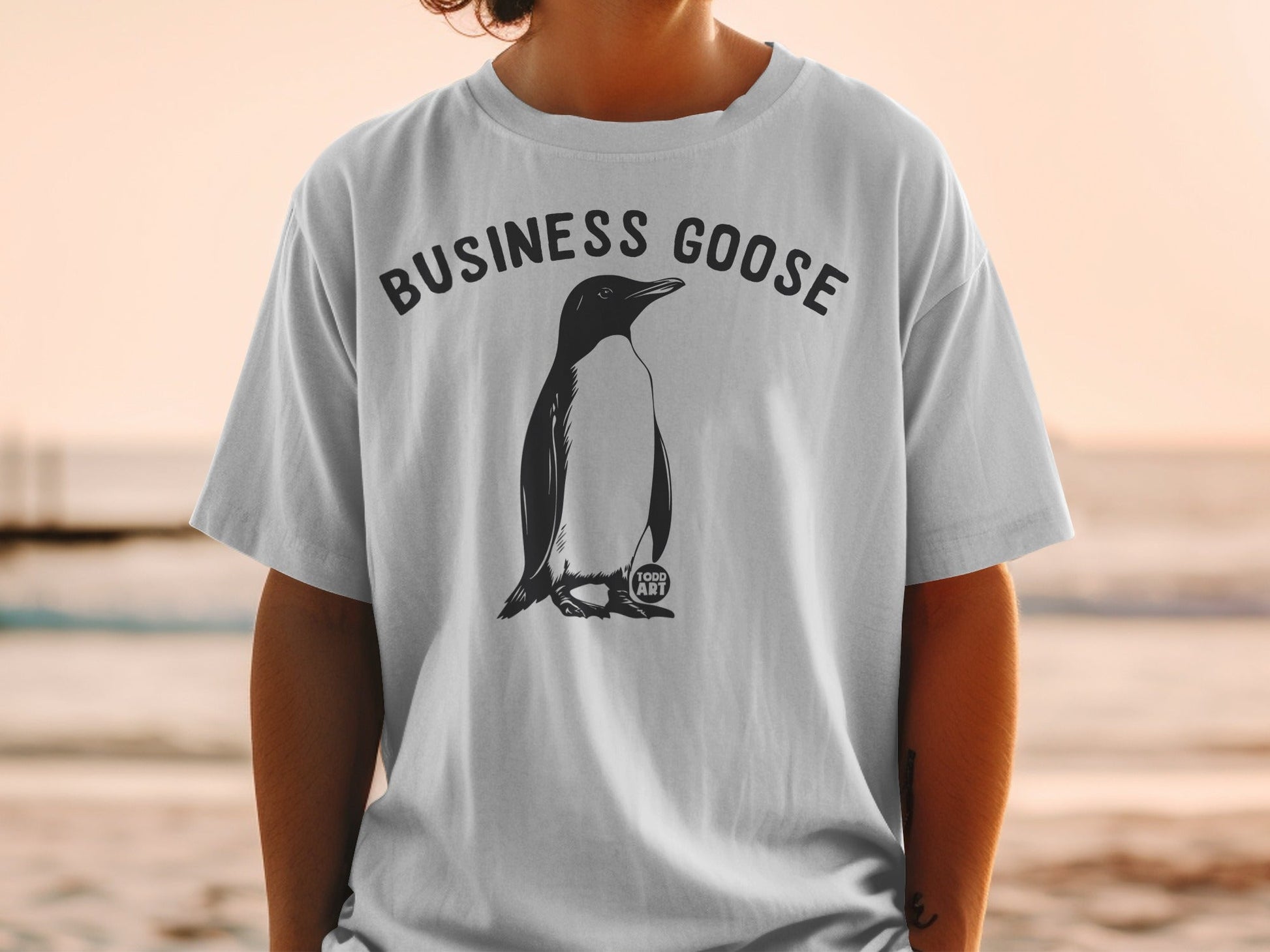 White t-shirt with a black penguin illustration and "BUSINESS GOOSE" text.
