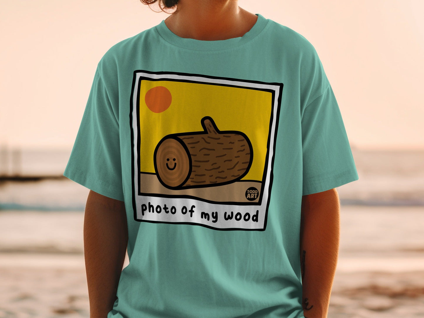Teal t-shirt with a cartoon wood log smiling inside a framed photo.