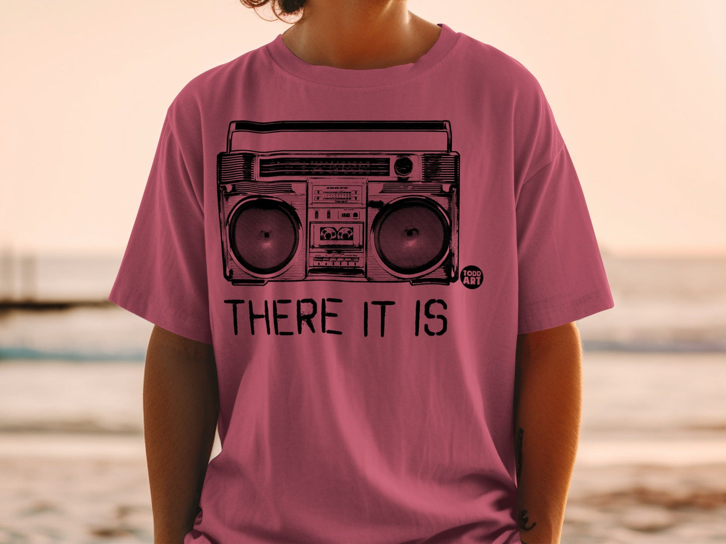Pink t-shirt with a graphic of a boombox and the text "THERE IT IS".