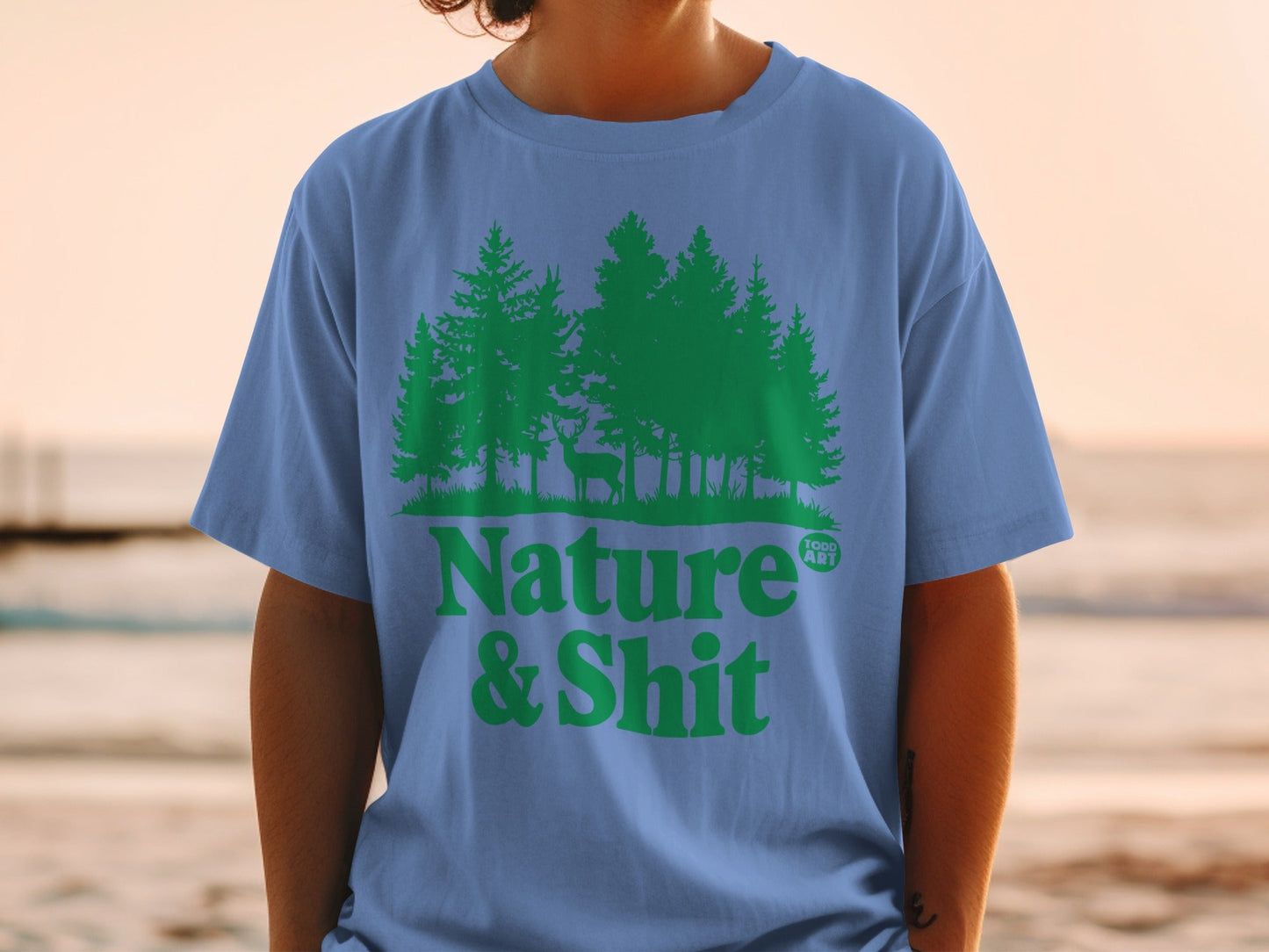 Blue t-shirt with green forest and deer graphic, text "Nature & Shit".