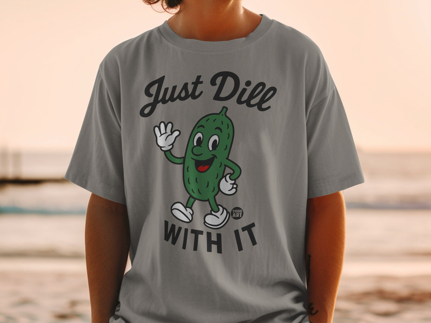 T-shirt with a cartoon pickle waving, saying "Just Dill With It".