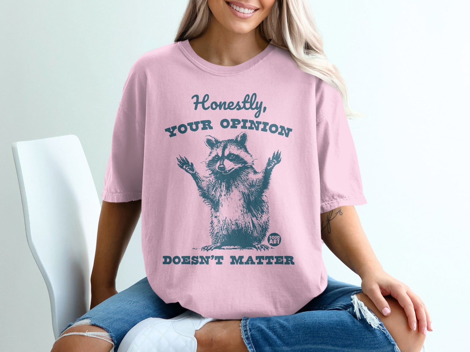 Pink t-shirt with raccoon graphic and text "HONESTLY, YOUR OPINION DOESN'T MATTER".