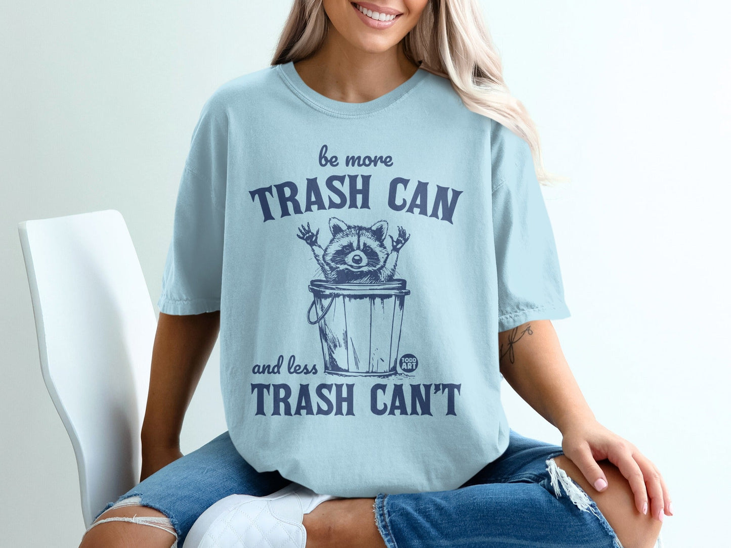 Light blue t-shirt with raccoon in trash can graphic and "be more TRASH CAN and less TRASH CAN'T" text.
