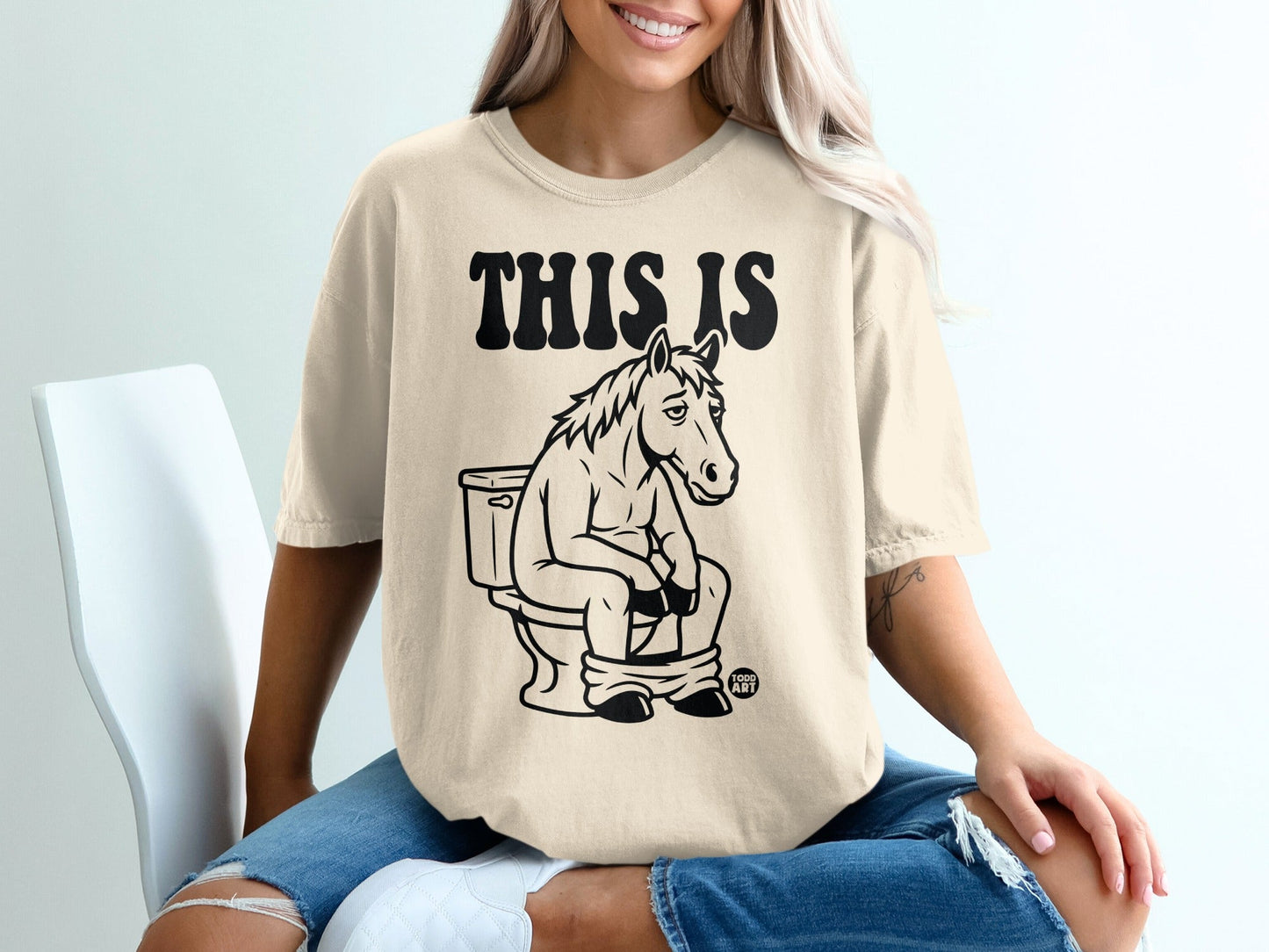 Horse sitting on toilet on tan t-shirt, text "THIS IS".