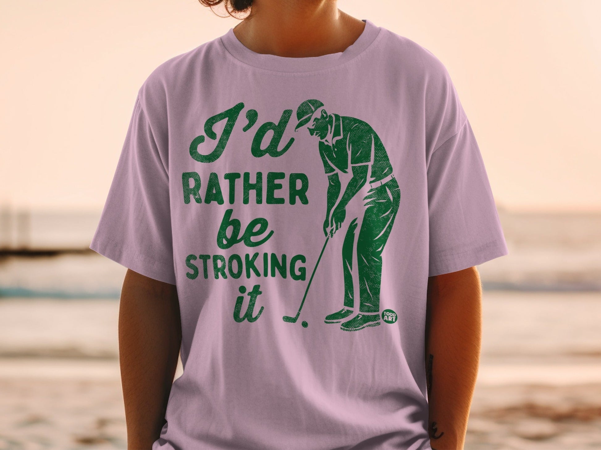 Purple t-shirt with green text saying "I'd rather be stroking it" and a golfer graphic.