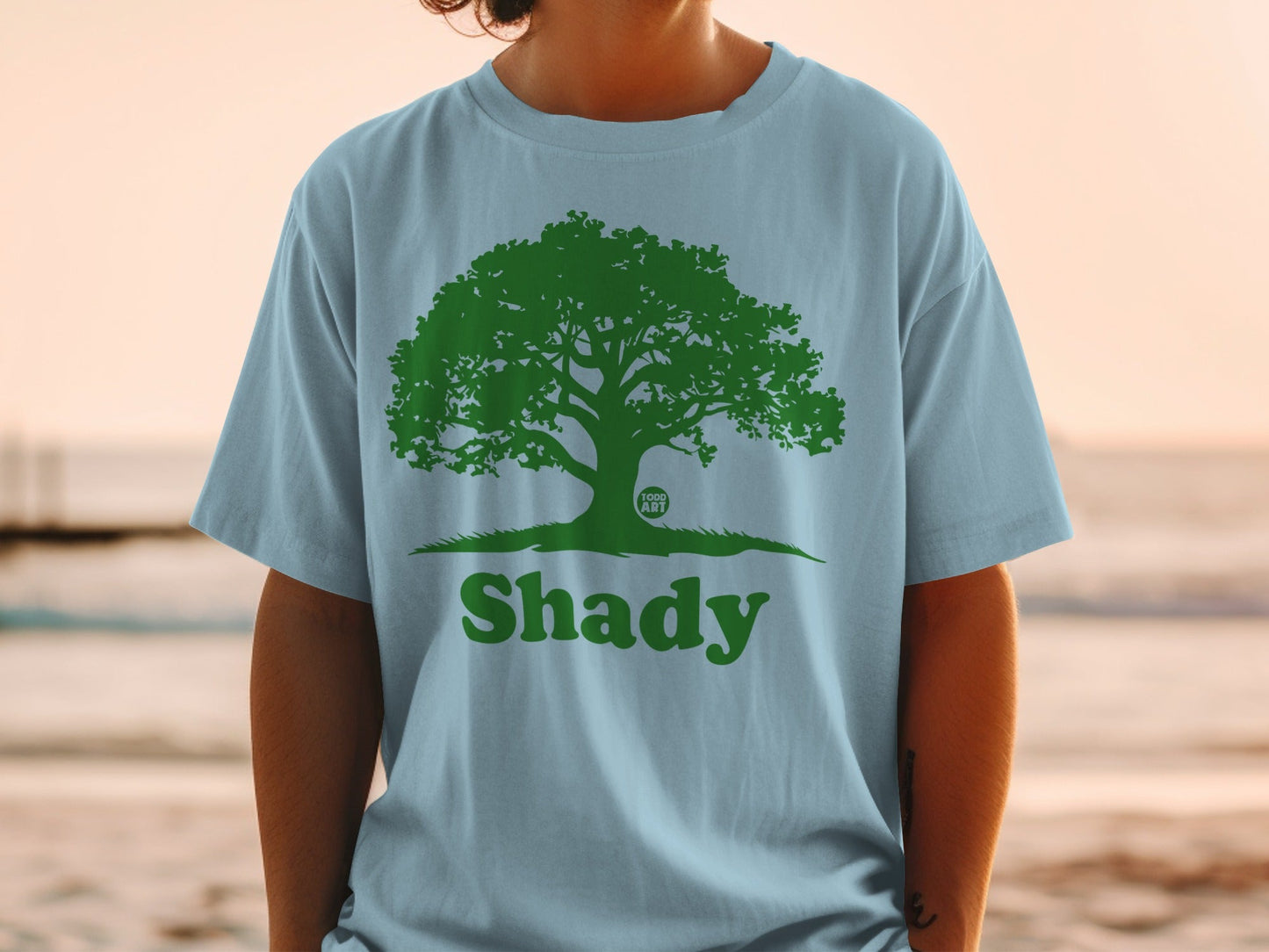 Light blue t-shirt with a green tree and "Shady" text graphic.