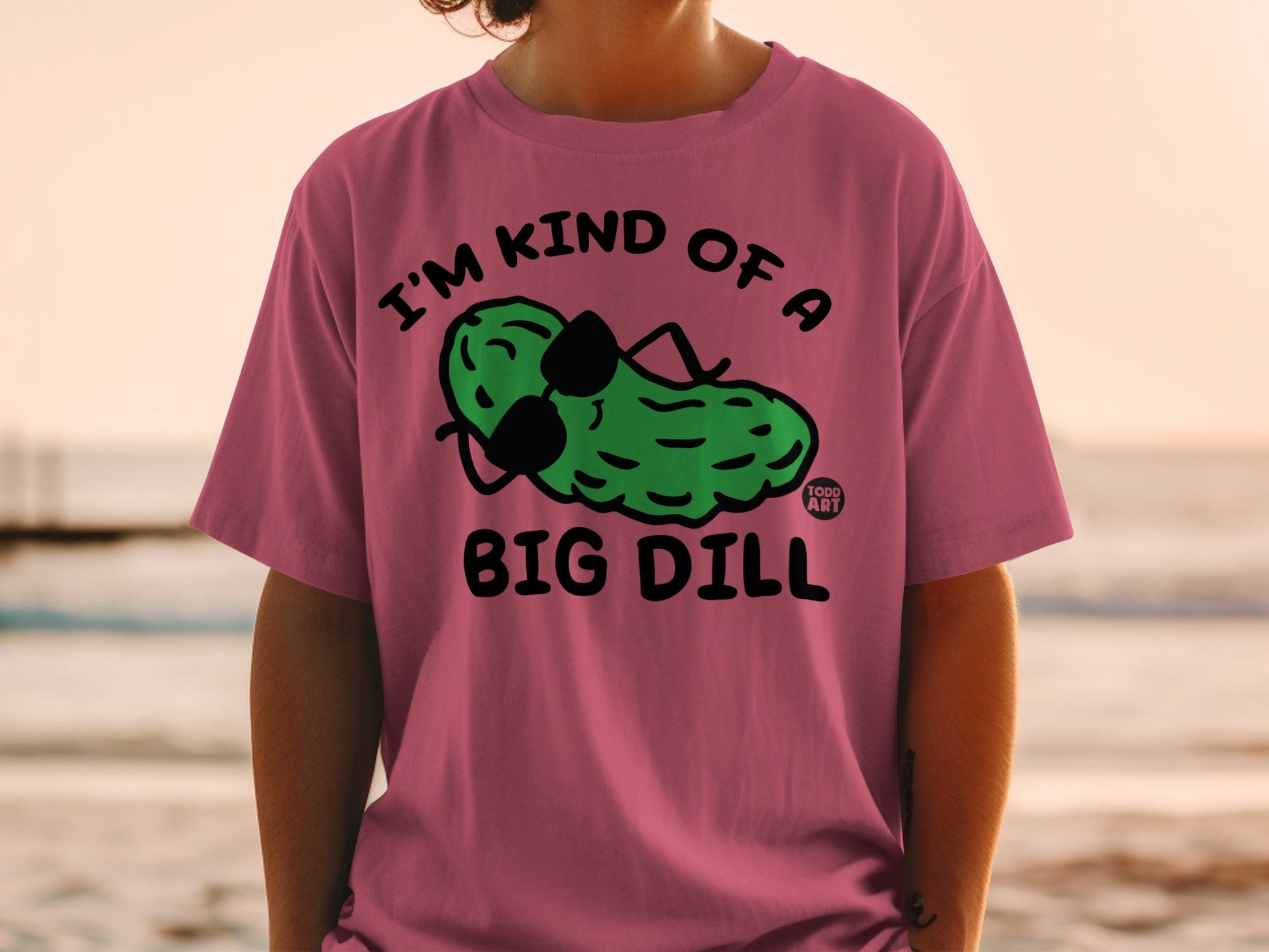 Pink t-shirt with cartoon pickle wearing sunglasses, "I'M KIND OF A BIG DILL" text.