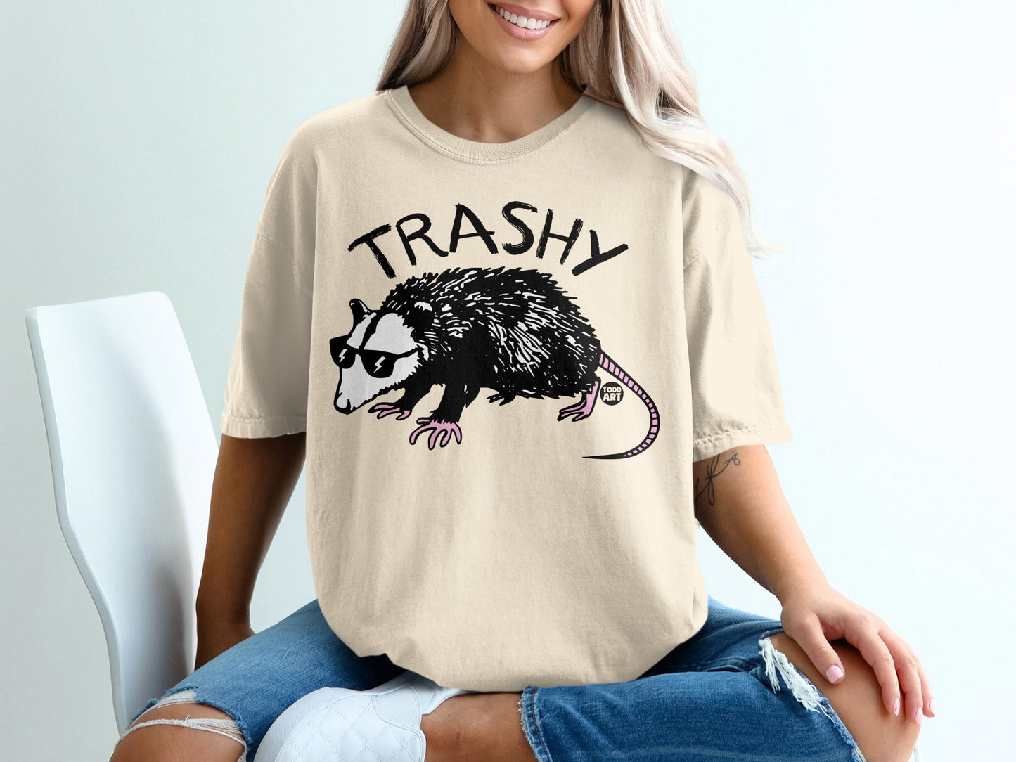 Opossum wearing sunglasses on a graphic t-shirt that says "TRASHY".