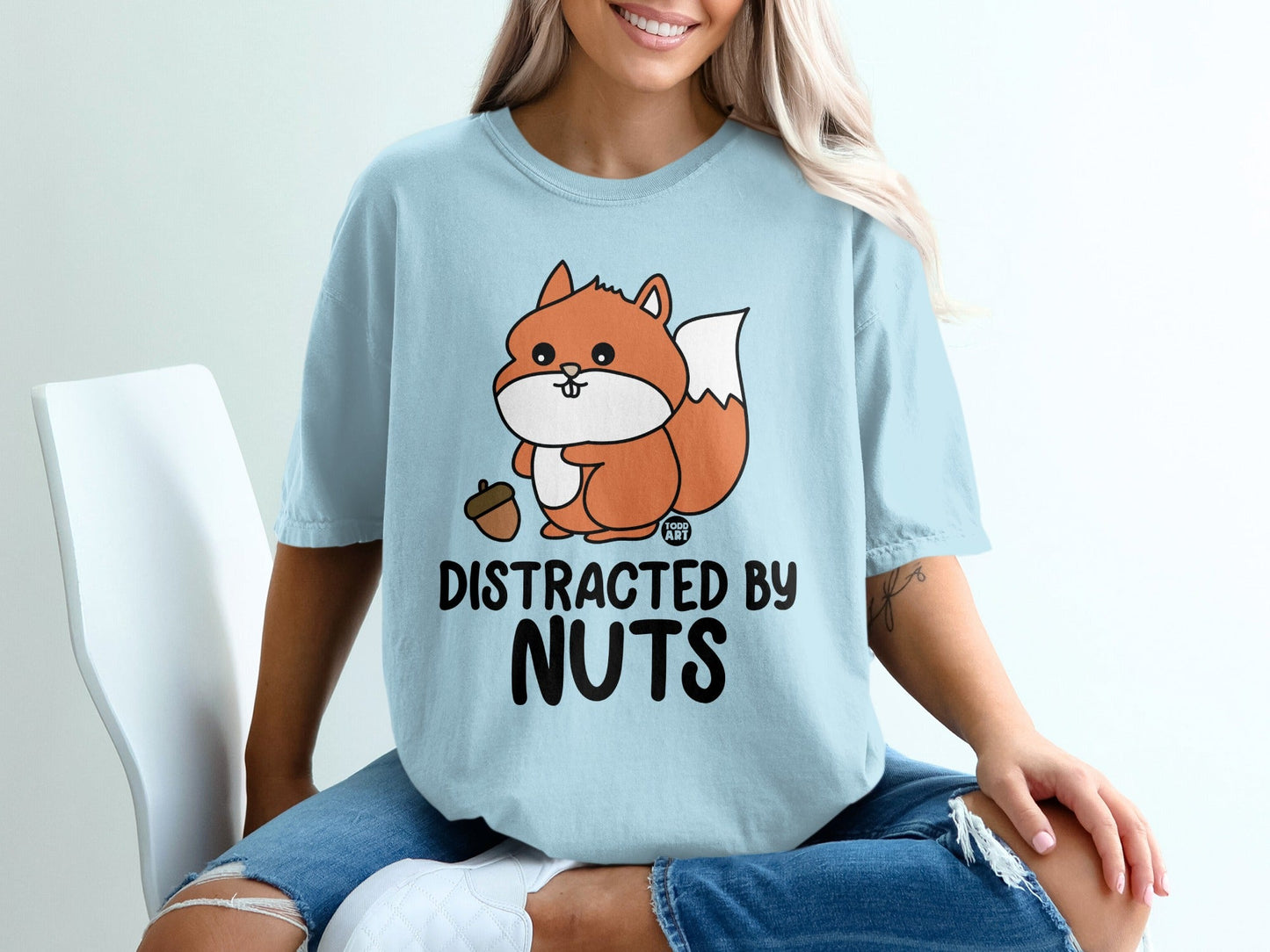 Light blue t-shirt with a cartoon squirrel holding an acorn, saying "Distracted by Nuts".