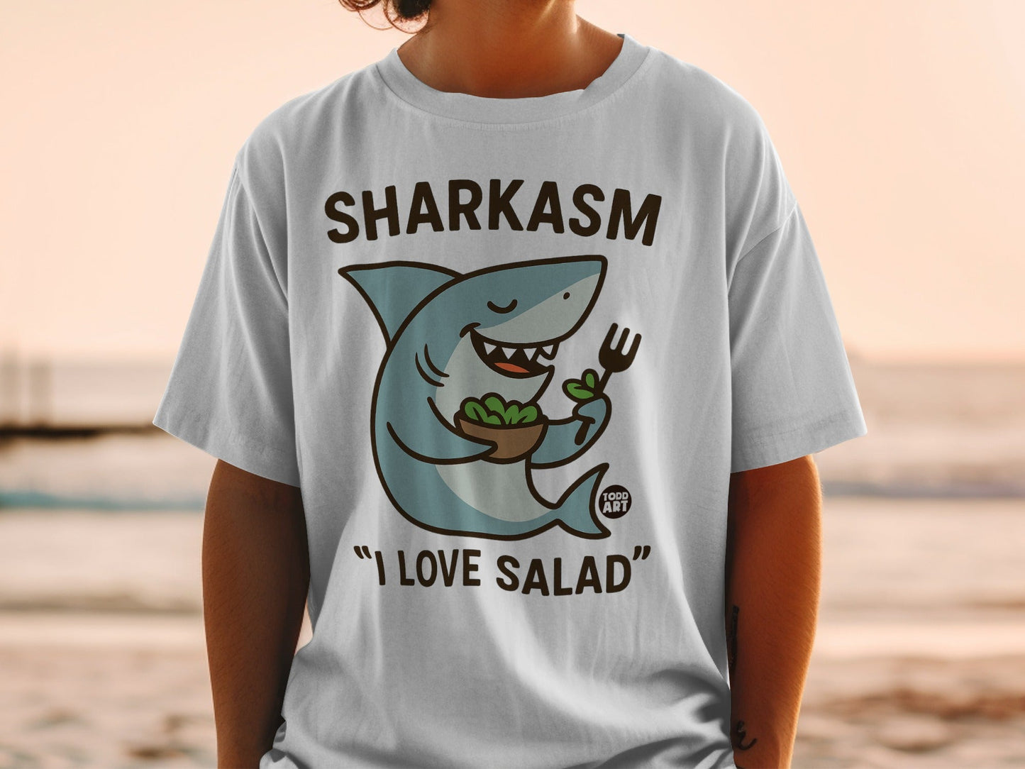 T-shirt with a cartoon shark holding a fork and salad, reading "Sharkasm I Love Salad".
