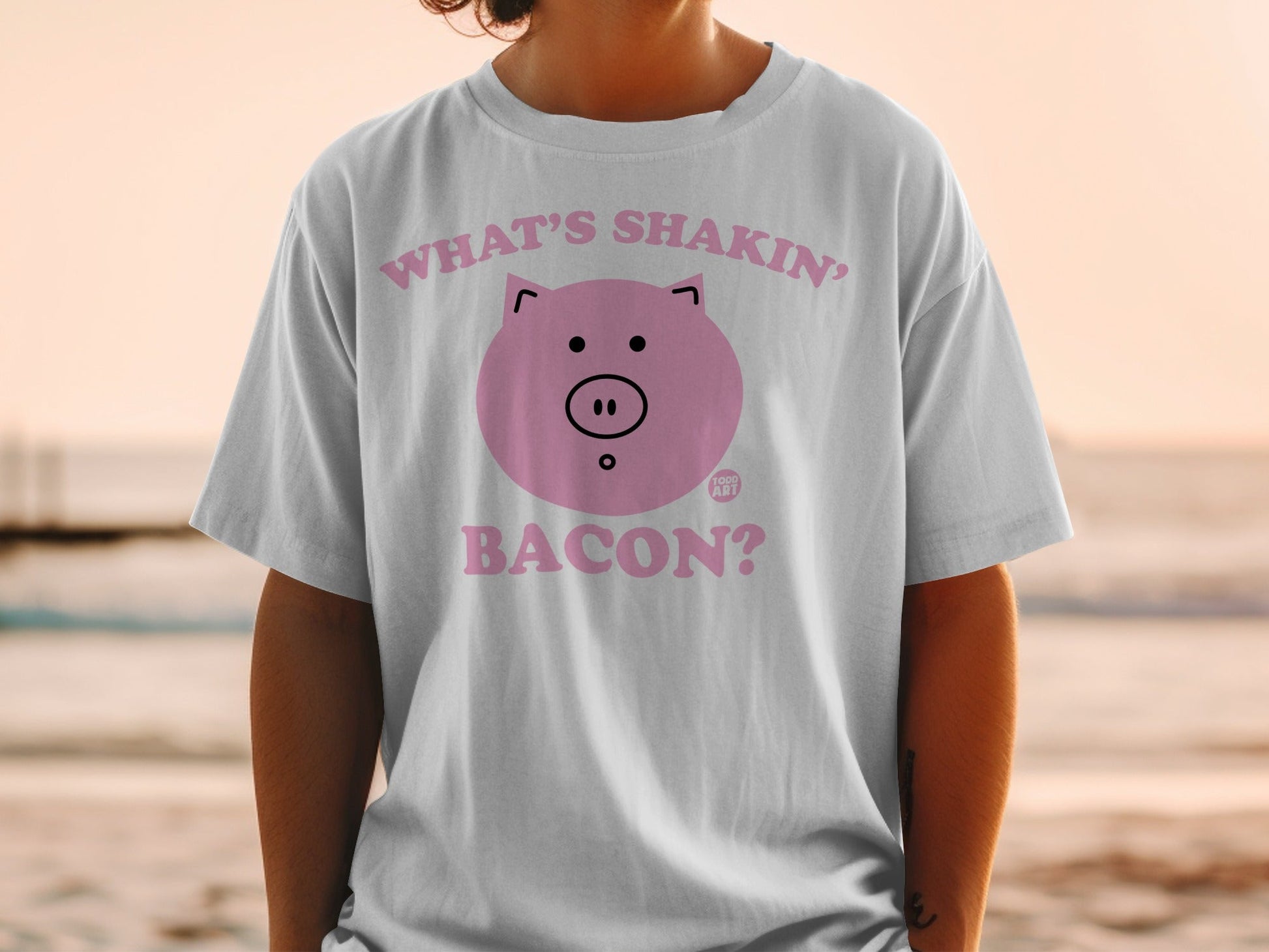 White t-shirt with pink pig graphic and "What's shakin'? Bacon?" text.