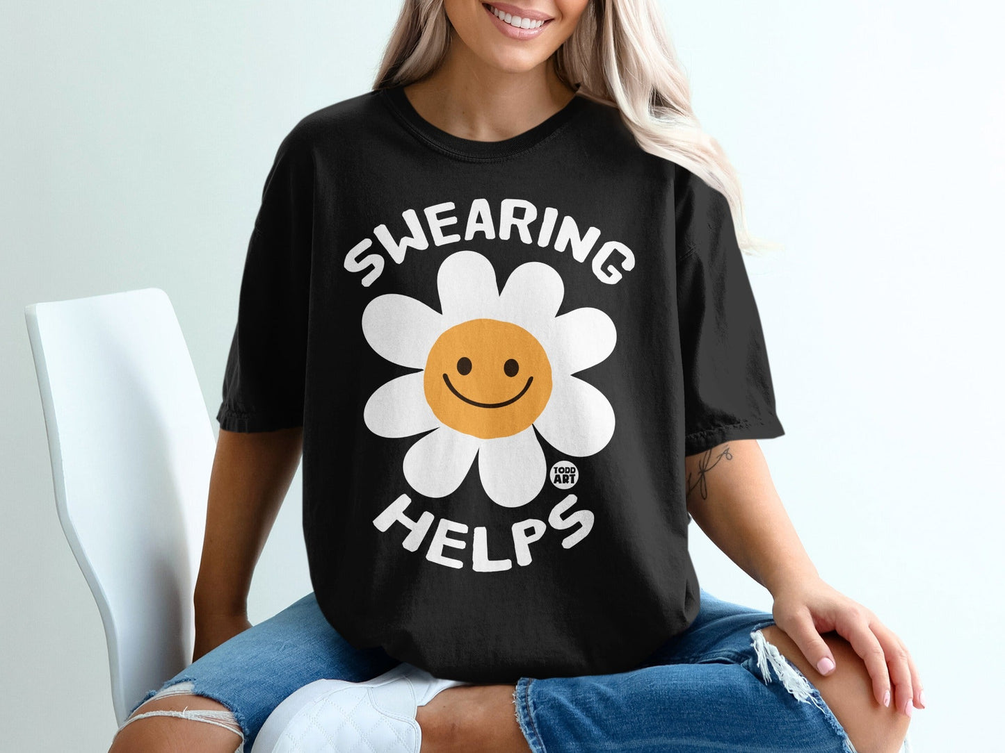 Black t-shirt with a smiling daisy and the text "SWEARING HELPS".