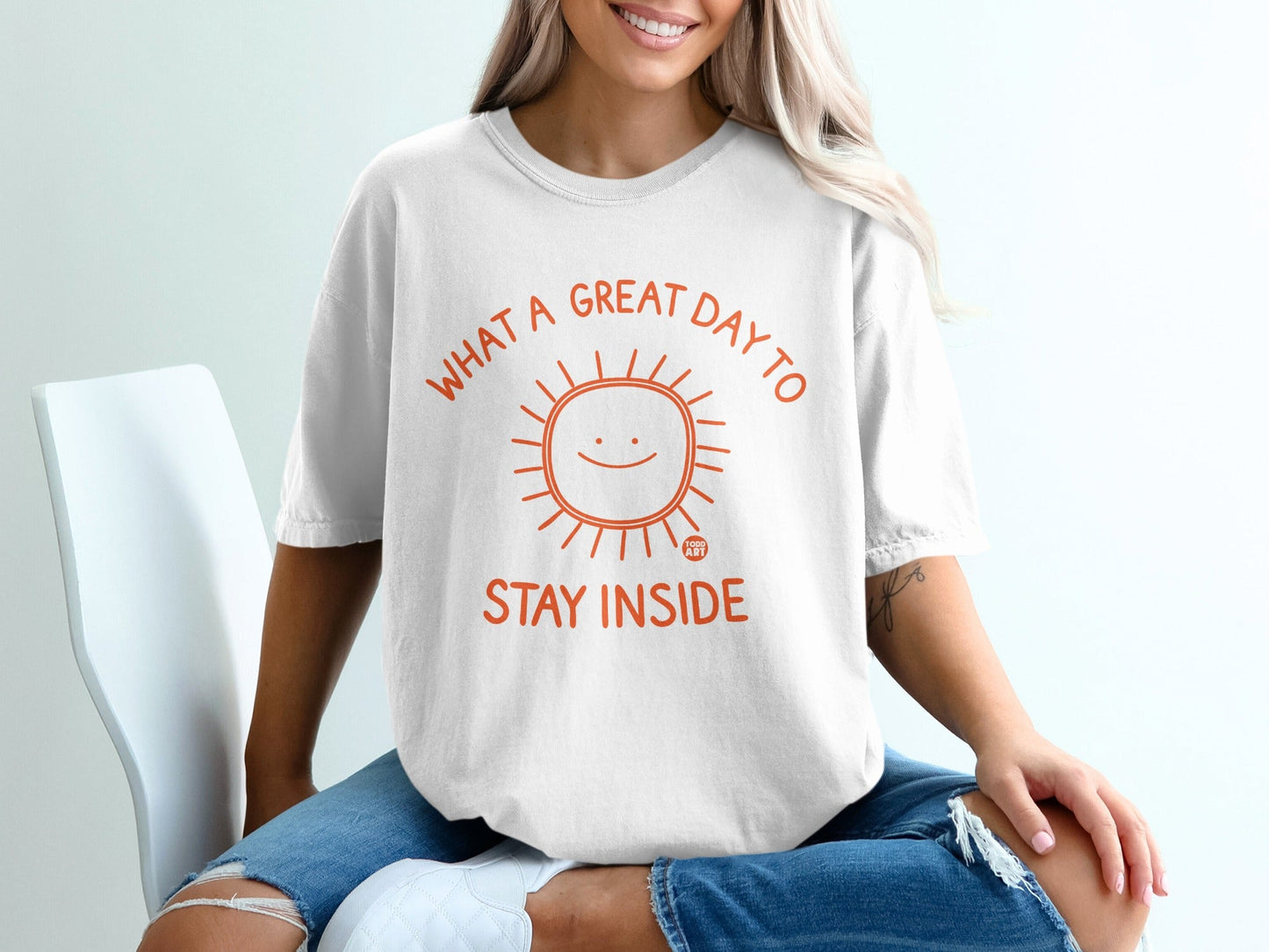 White t-shirt with an orange sun graphic and text "What a great day to stay inside."