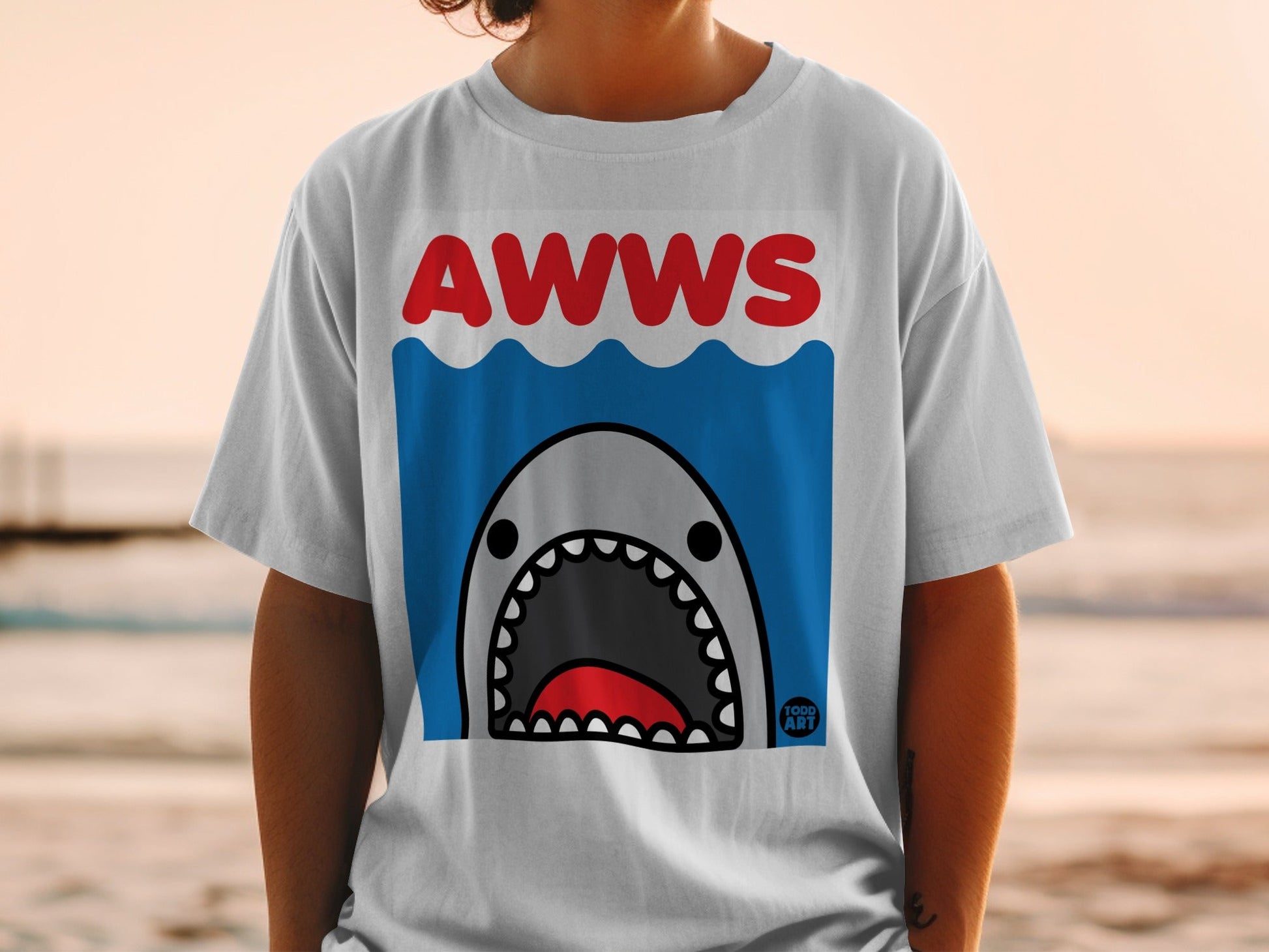 White t-shirt with cartoon shark and "AWWS" text on blue waves.
