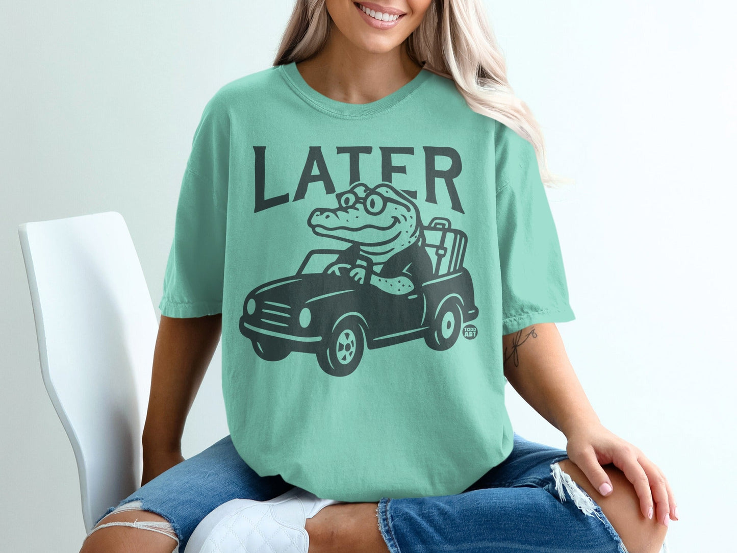 Green t-shirt with graphic of alligator driving a car, text "LATER" above.