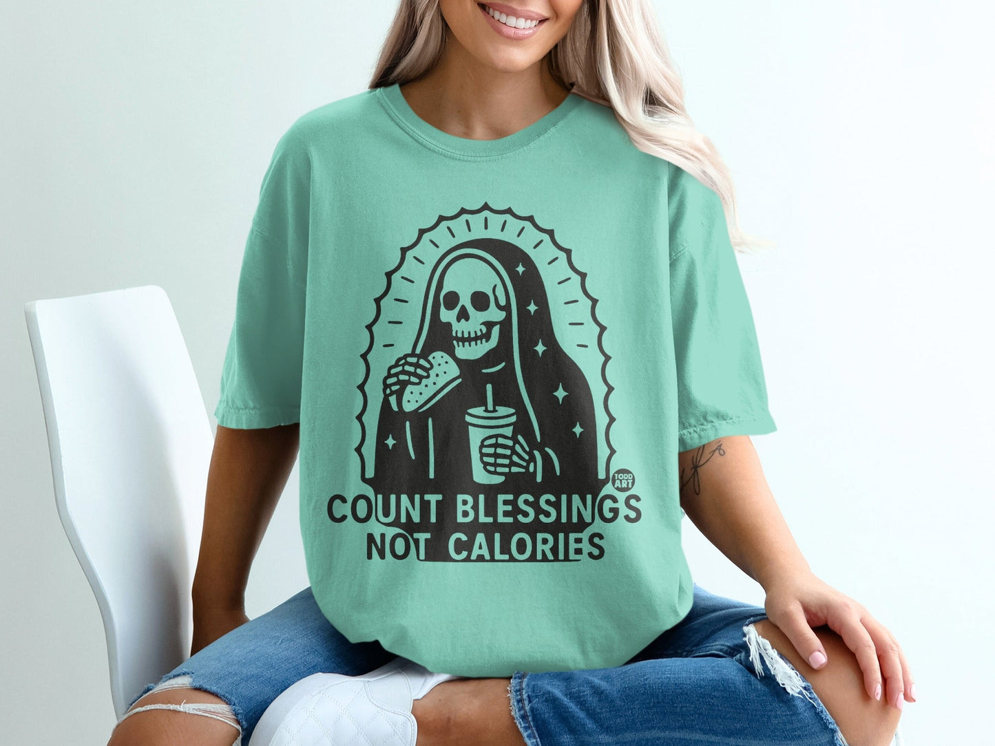 Teal t-shirt with skeleton holding a burger and drink, text "COUNT BLESSINGS NOT CALORIES".