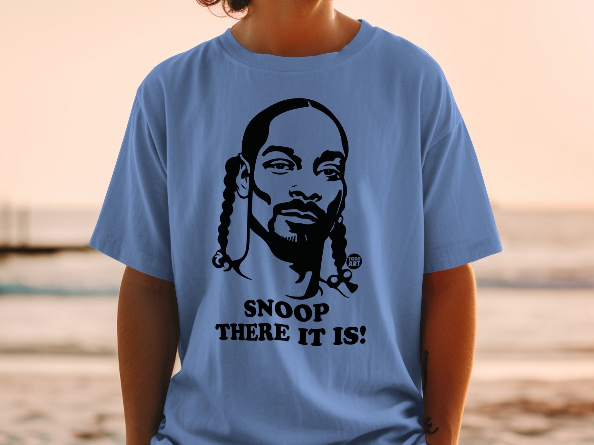 Blue t-shirt with black graphic of Snoop Dogg and text "SNOOP THERE IT IS!".