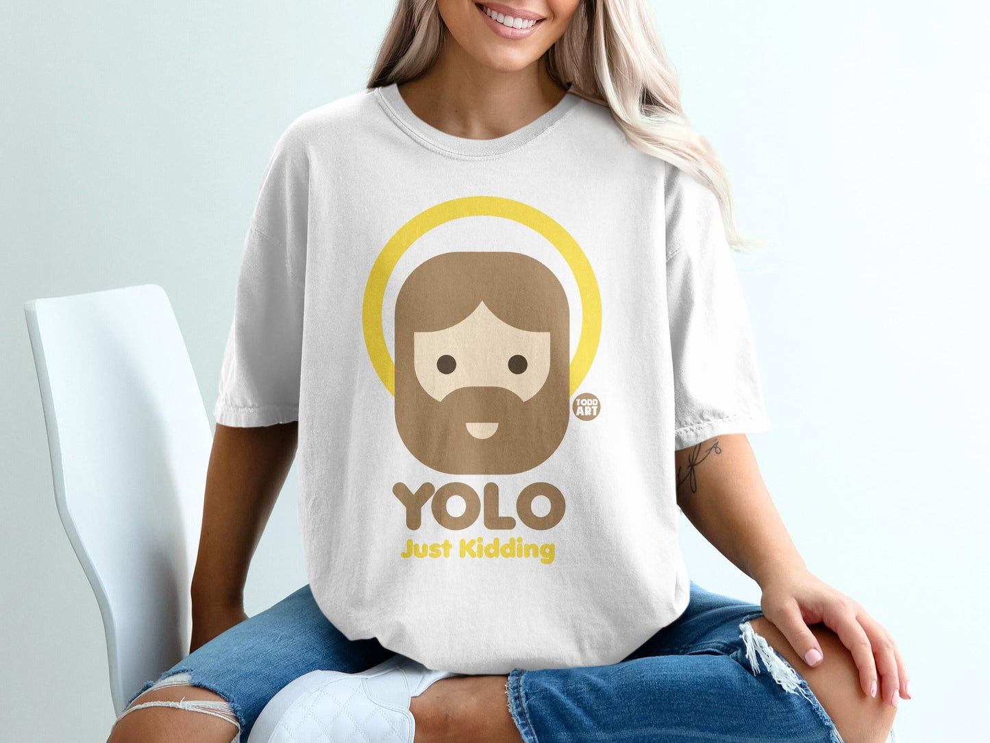 White t-shirt with "YOLO Just Kidding" graphic and cartoon haloed figure.